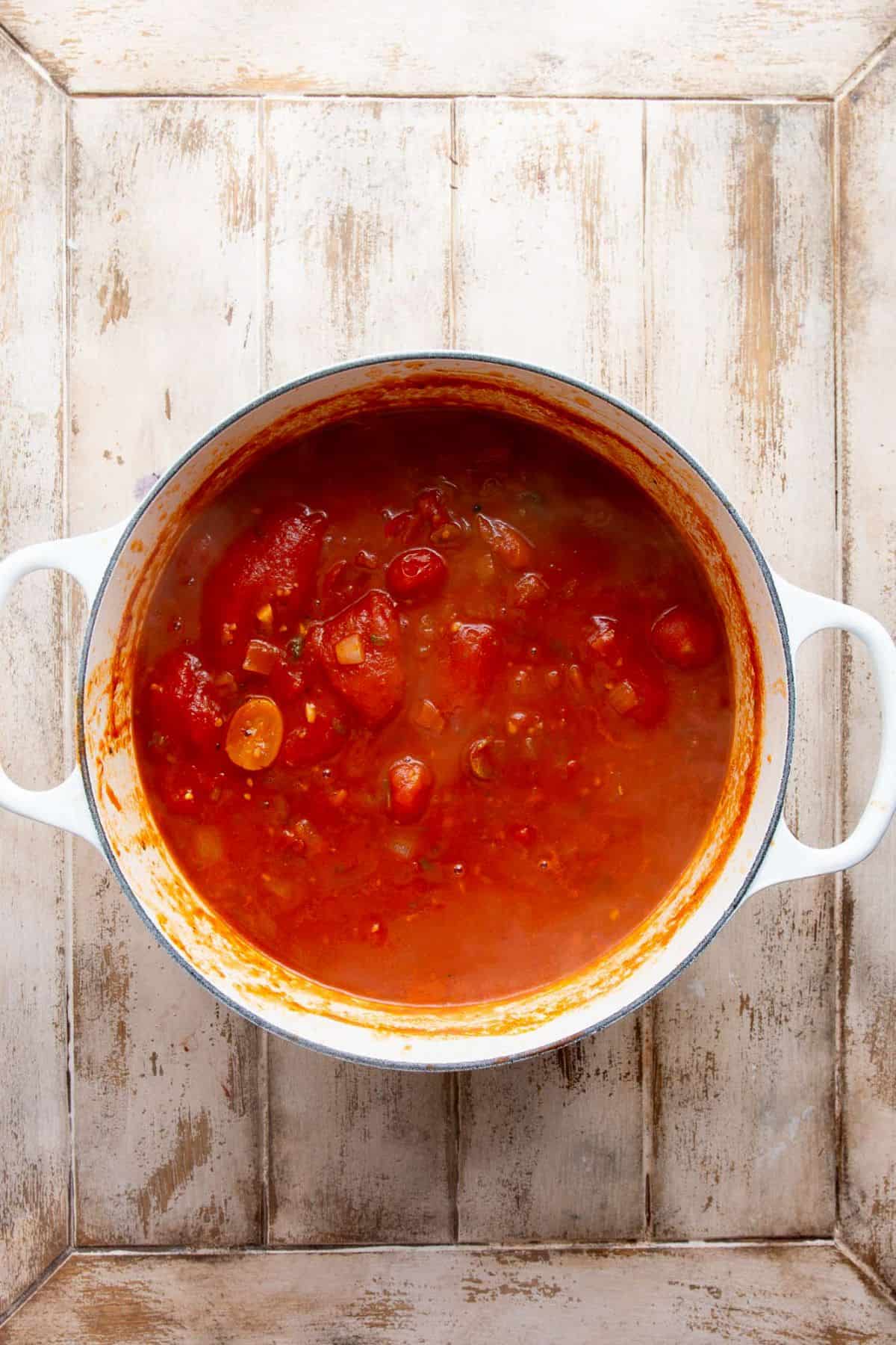 Crushed tomatoes and broth added to the cherry tomatoes and onion, simmering in a white Dutch oven before blending.