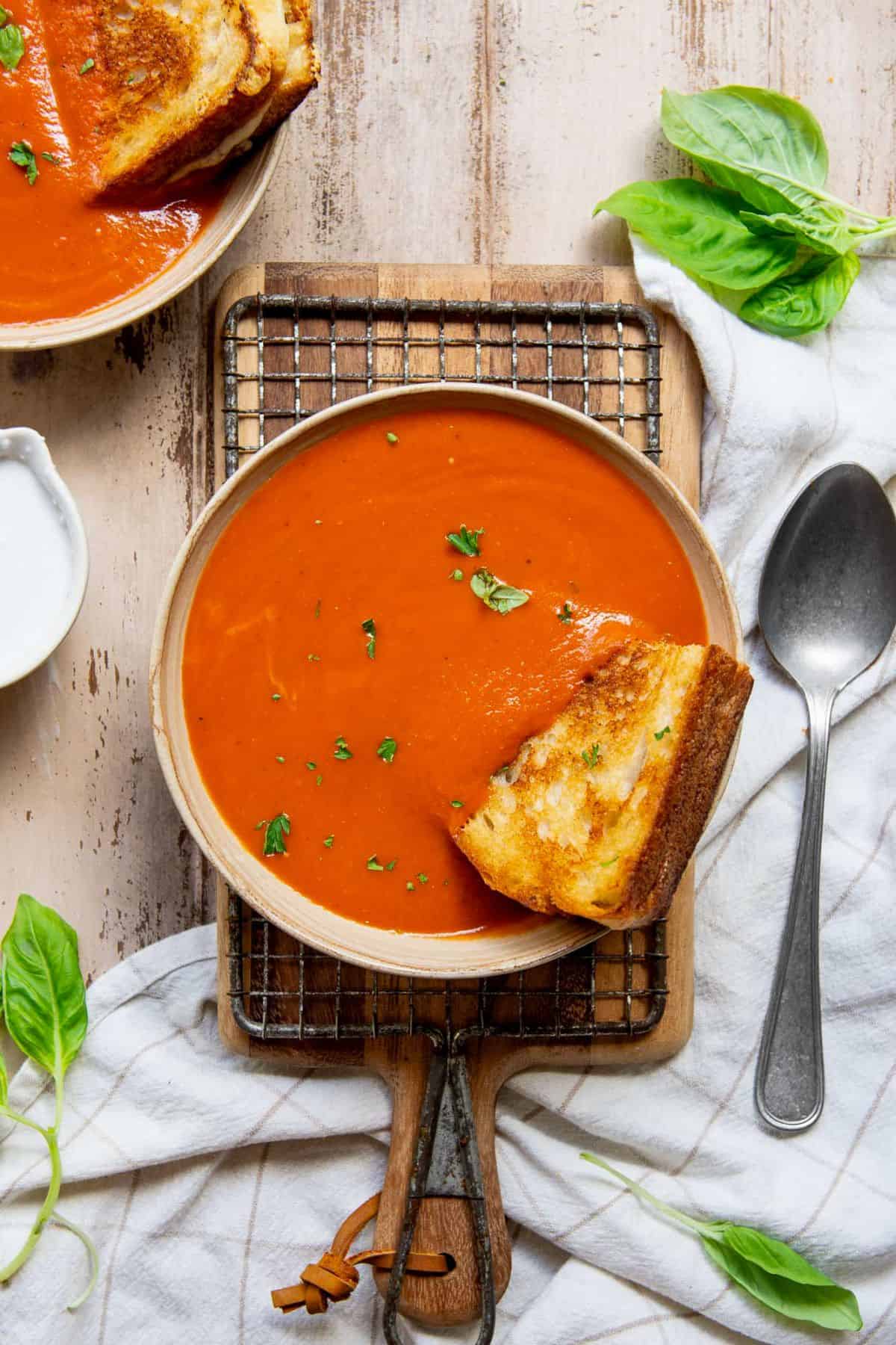 Bowl of creamy dairy free tomato soup topped with fresh basil and served with a grilled cheese sandwich.