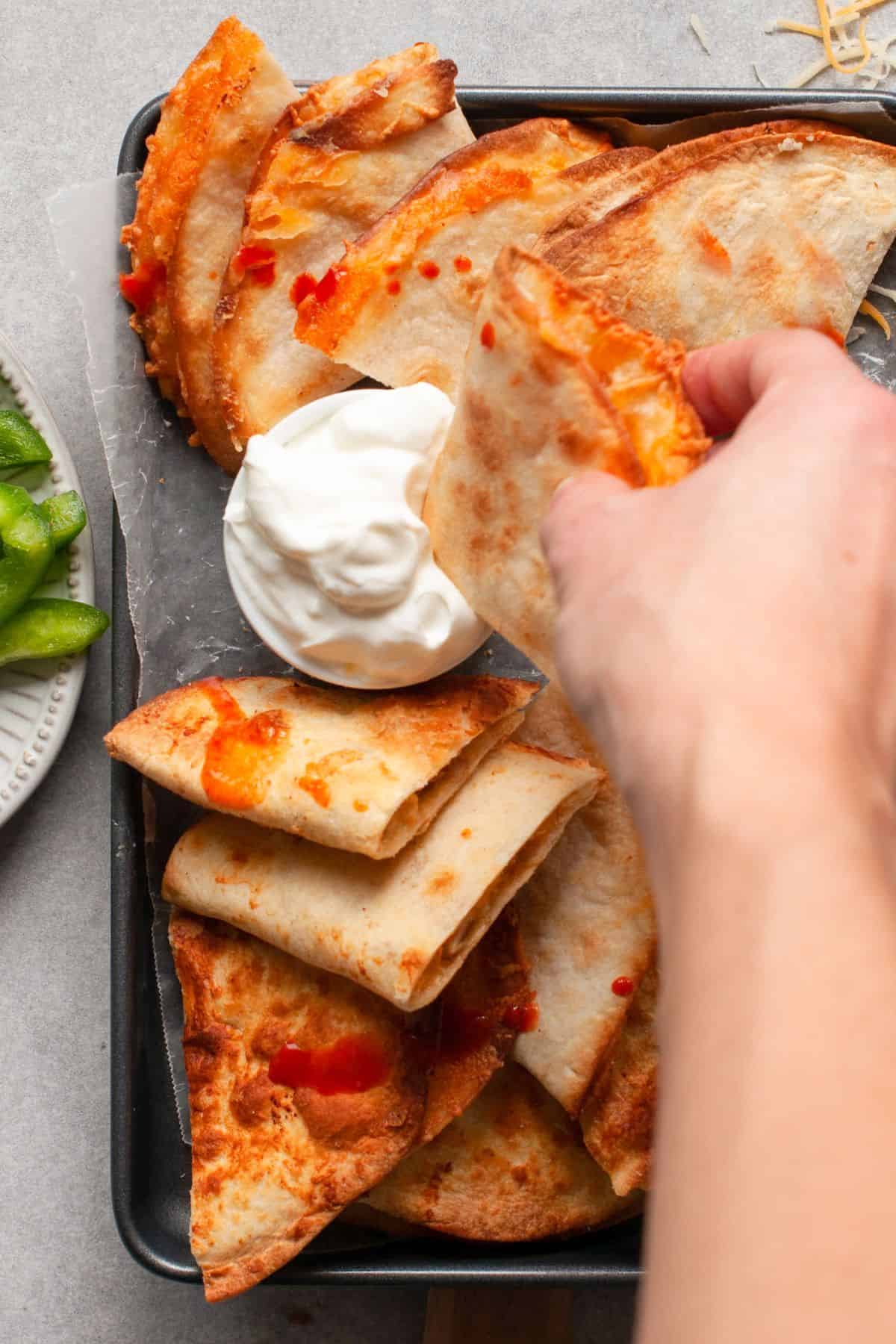 Hand dipping a crispy quesadilla wedge into sour cream.