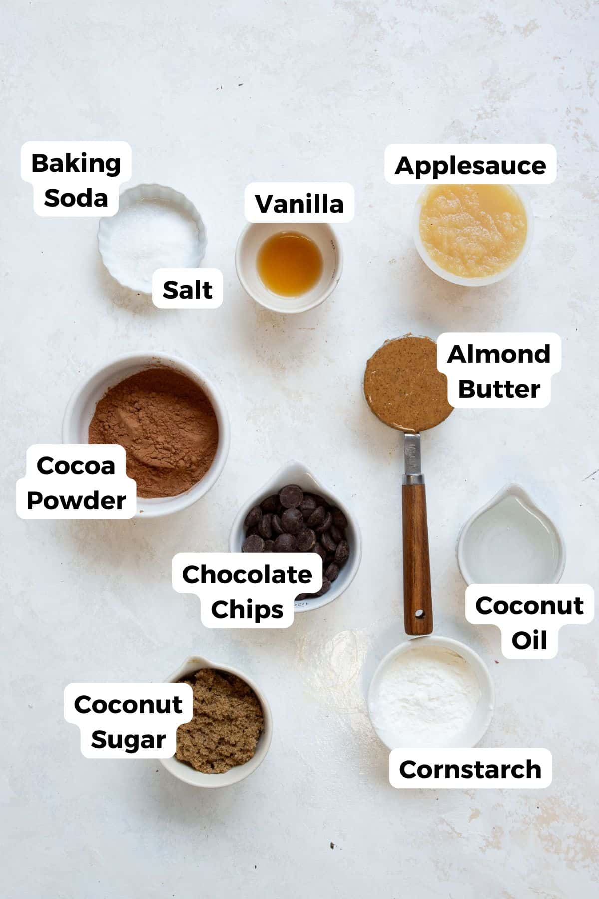 Labeled ingredients for a flourless brownie skillet including cocoa powder, almond butter, applesauce, coconut sugar, and chocolate chips.