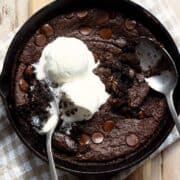 Flourless brownie skillet topped with vanilla ice cream and a spoon scooping out the gooey center.