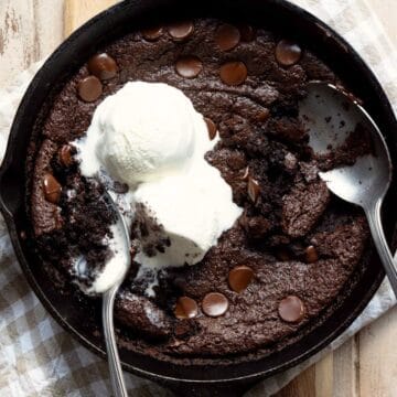 Flourless brownie skillet topped with vanilla ice cream and a spoon scooping out the gooey center.
