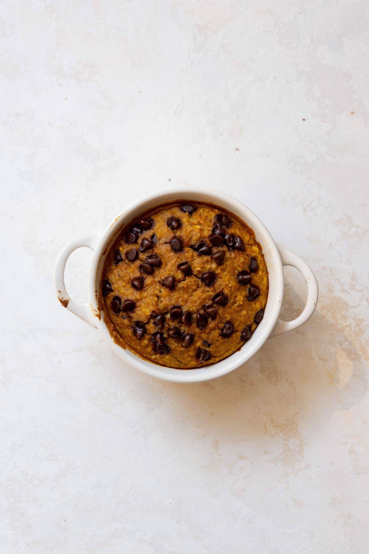 Baked pumpkin baked oats in a white ramekin with melted chocolate chips on top.