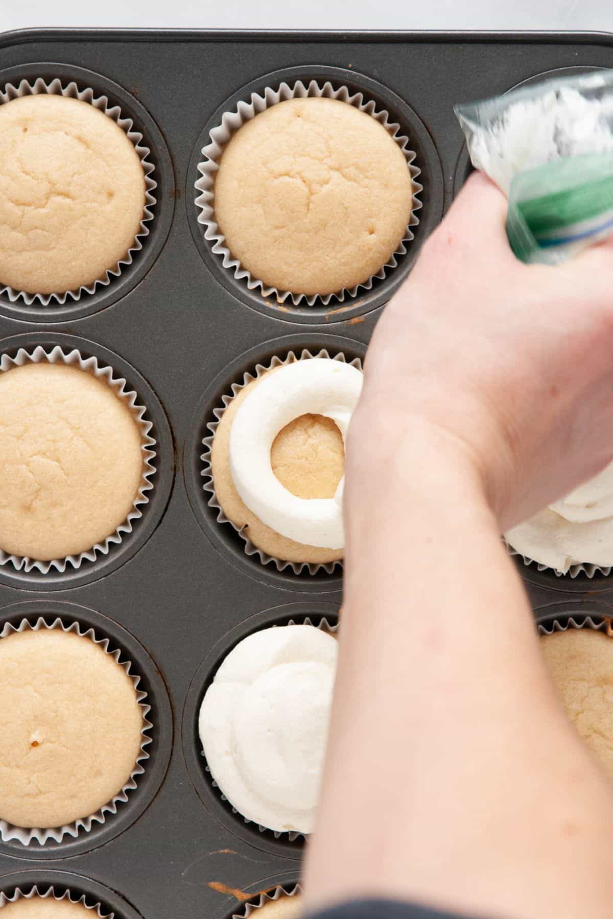 Piping vanilla buttercream onto cooled healthy vanilla cupcakes in the tin