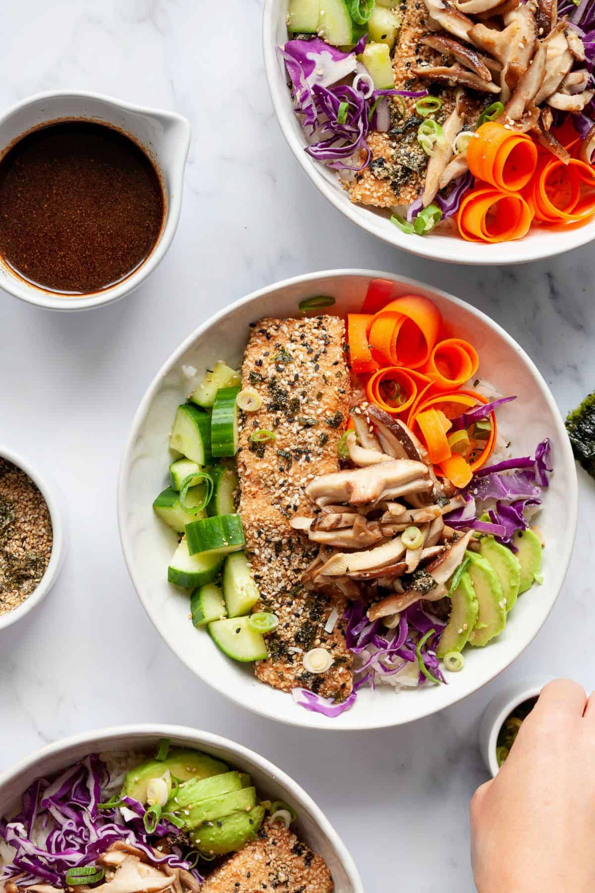 Three furikake salmon bowls with rice and vegetables.