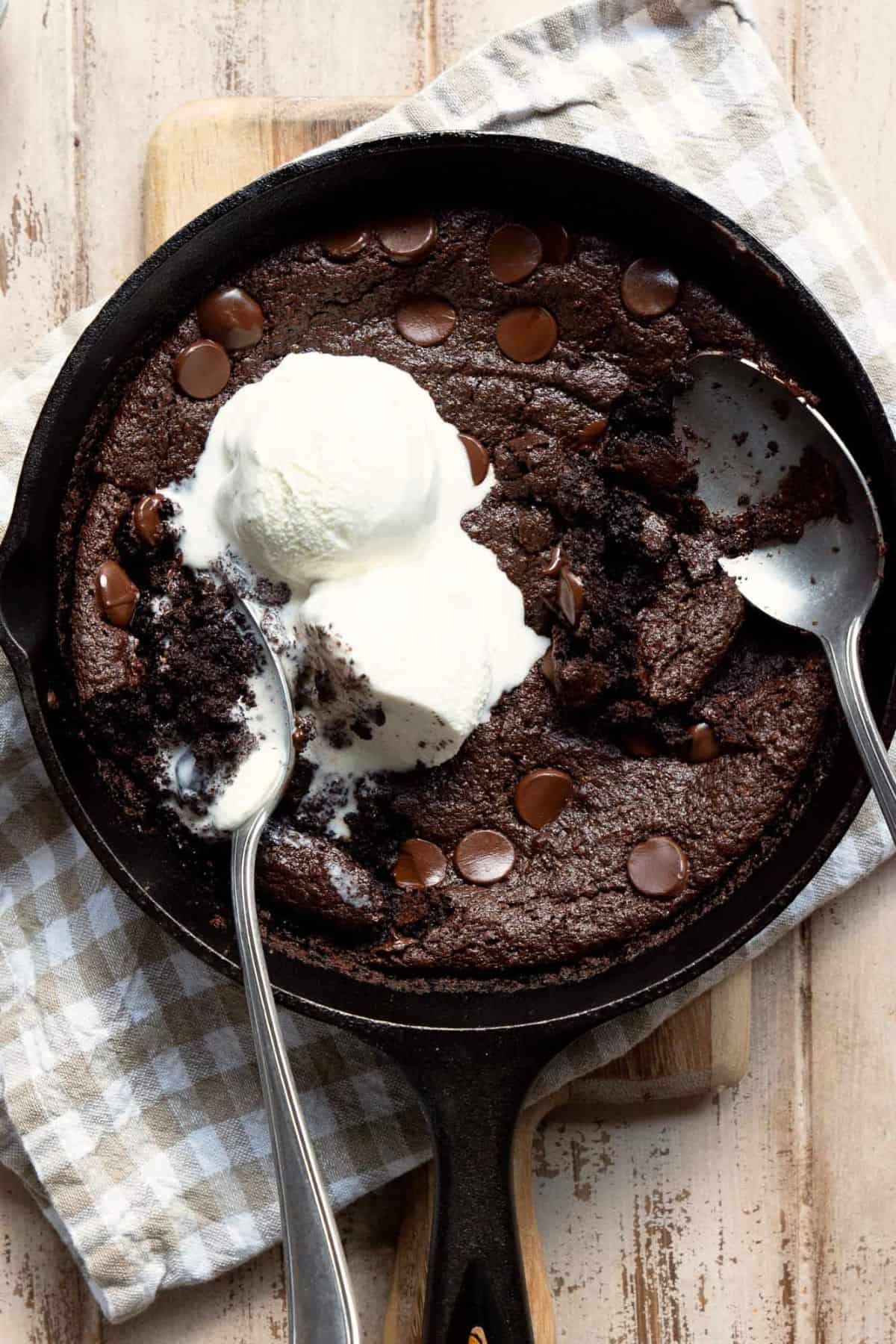 Gooey brownie skillet in a cast iron pan with two scoops of vanilla ice cream.