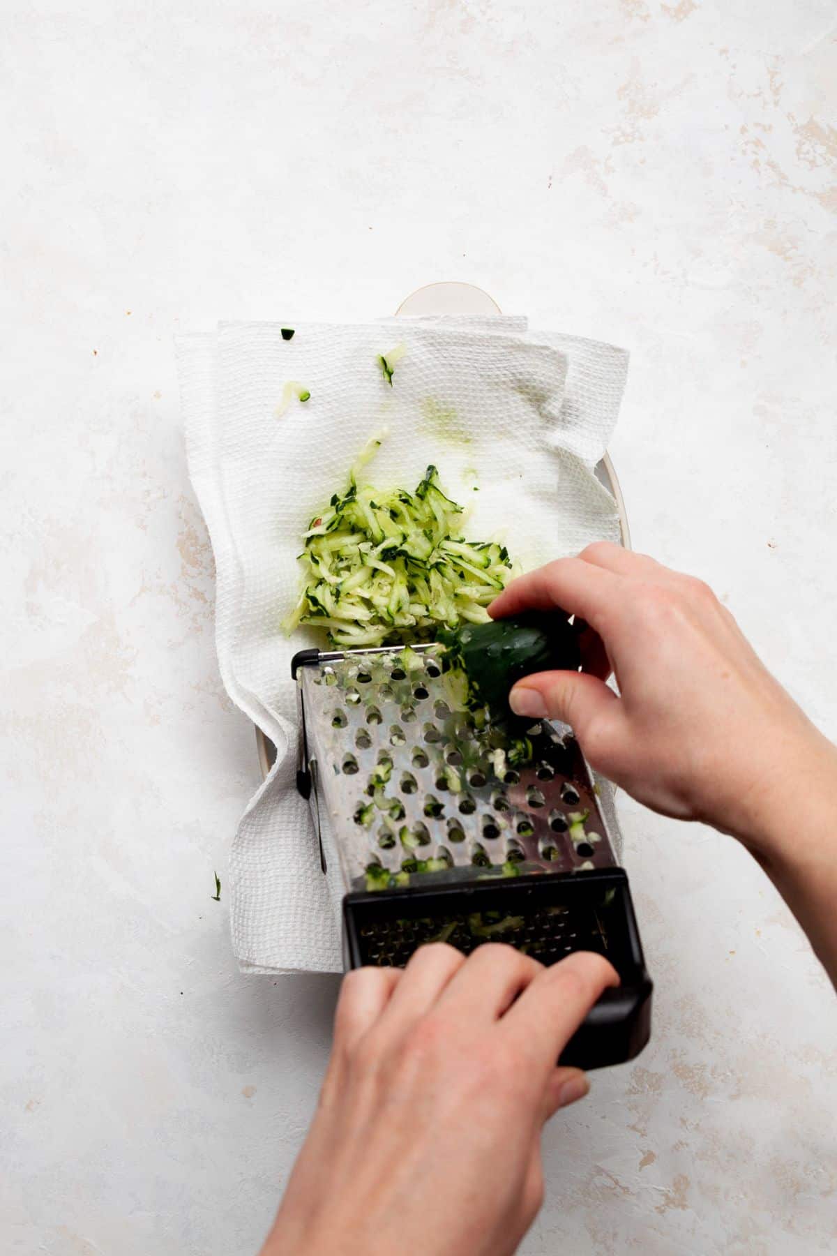 Grating cucumber on a box grater over a kitchen towel.