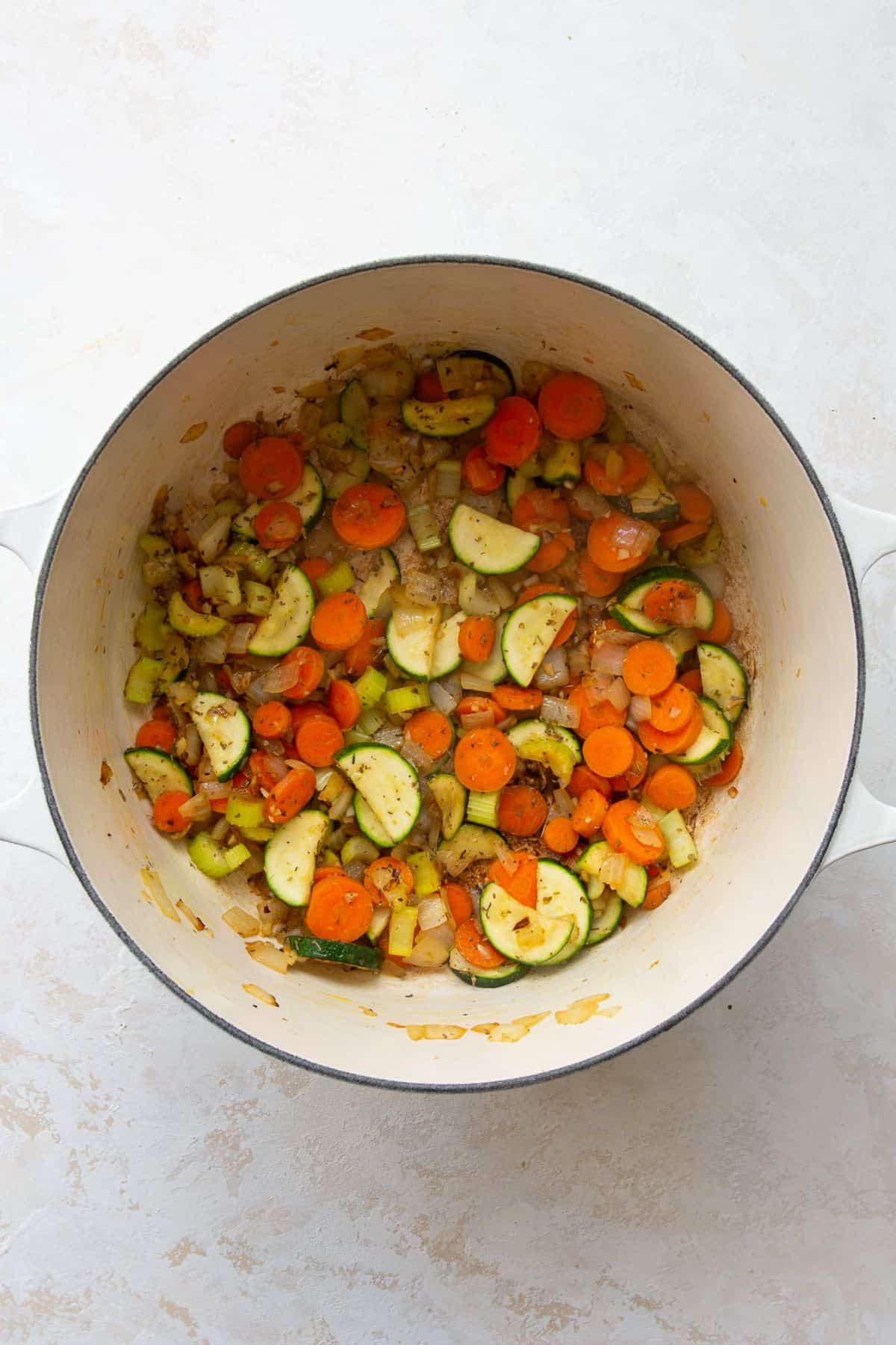 Sautéed onion, carrots, celery, and zucchini in a white Dutch oven.