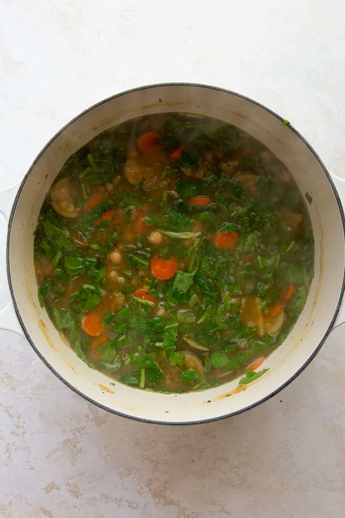Spinach and parsley stirred into Greek chickpea soup in a pot.