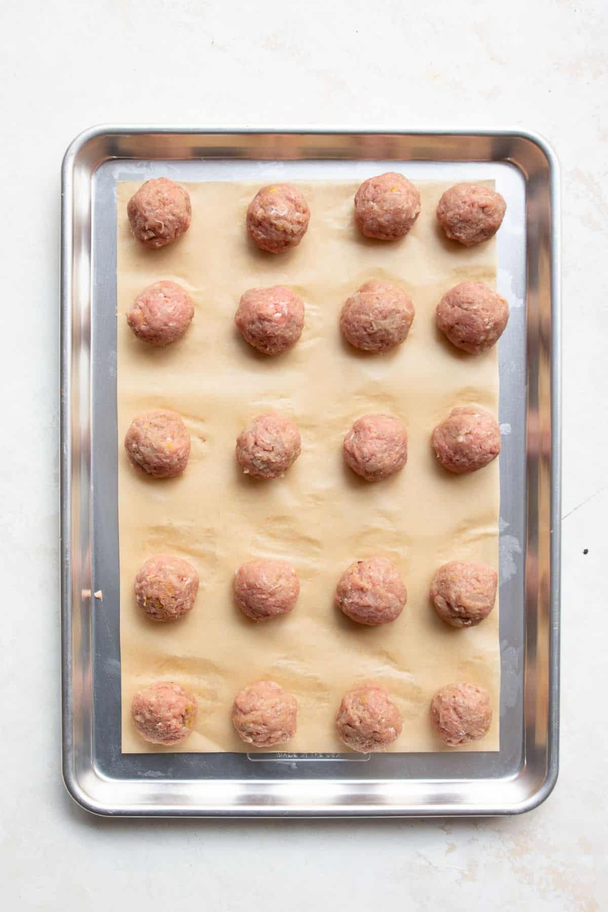 Twenty raw Greek turkey meatballs rolled and spaced on a parchment-lined baking sheet.