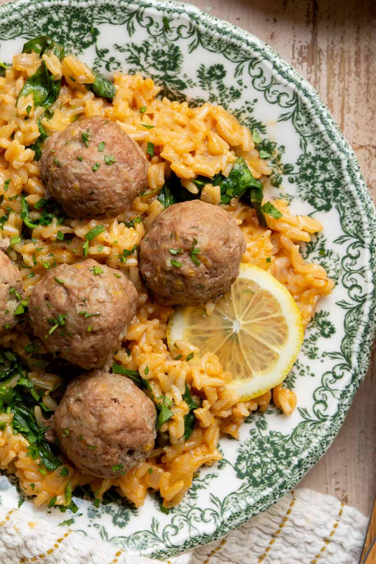 Close-up of Greek turkey meatballs on creamy lemon rice with fresh parsley and a lemon slice.