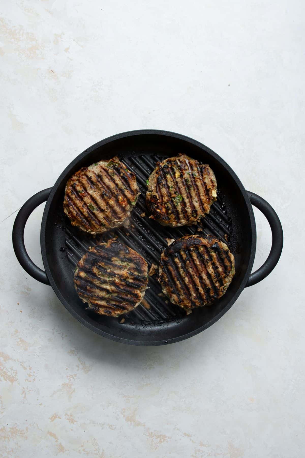 Four cooked Greek turkey burgers with dark grill marks in a black grill pan.