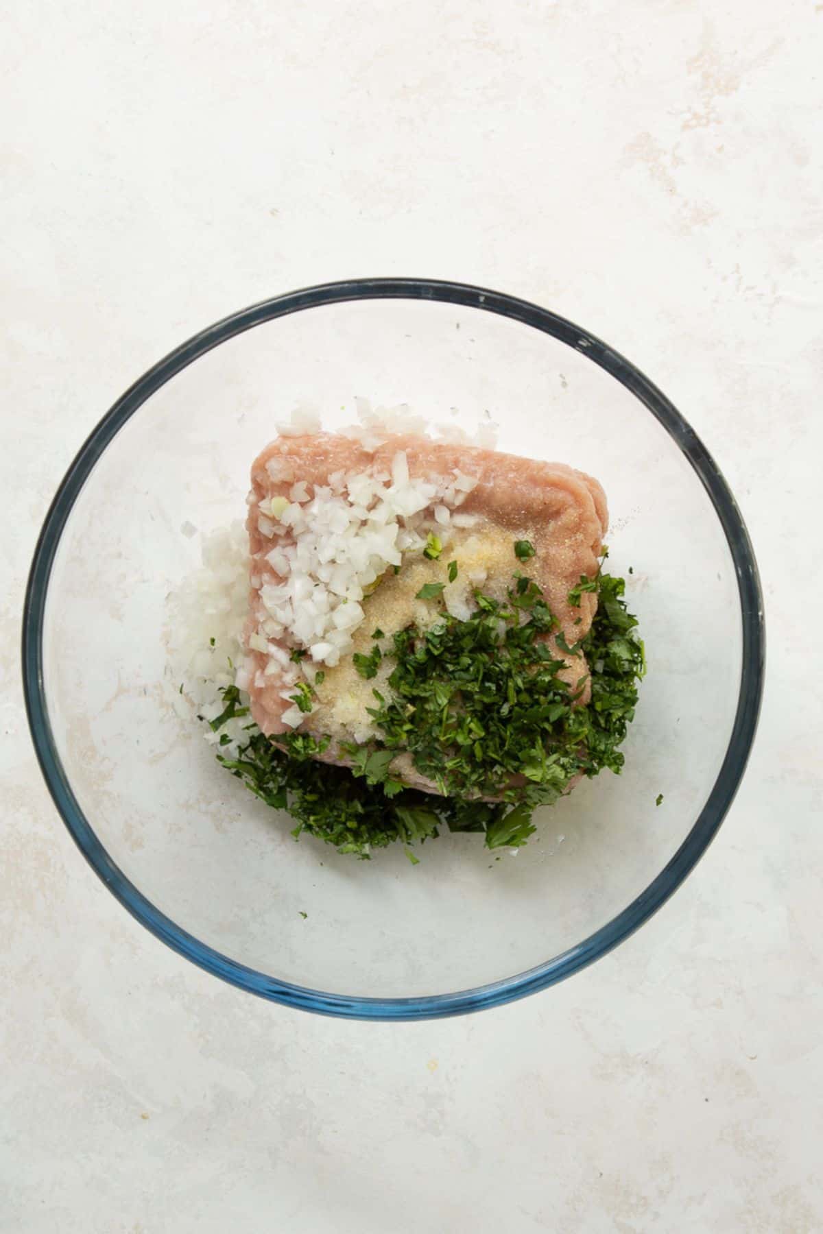 Ground chicken, onion, cilantro, and seasonings in a glass mixing bowl before mixing.