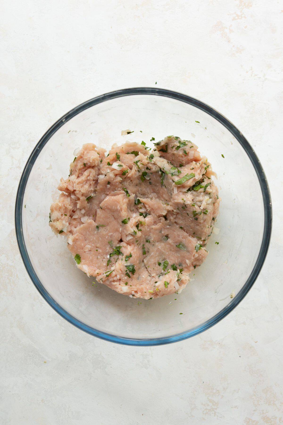 Ground chicken burger mixture combined with cilantro and onion in a glass bowl.