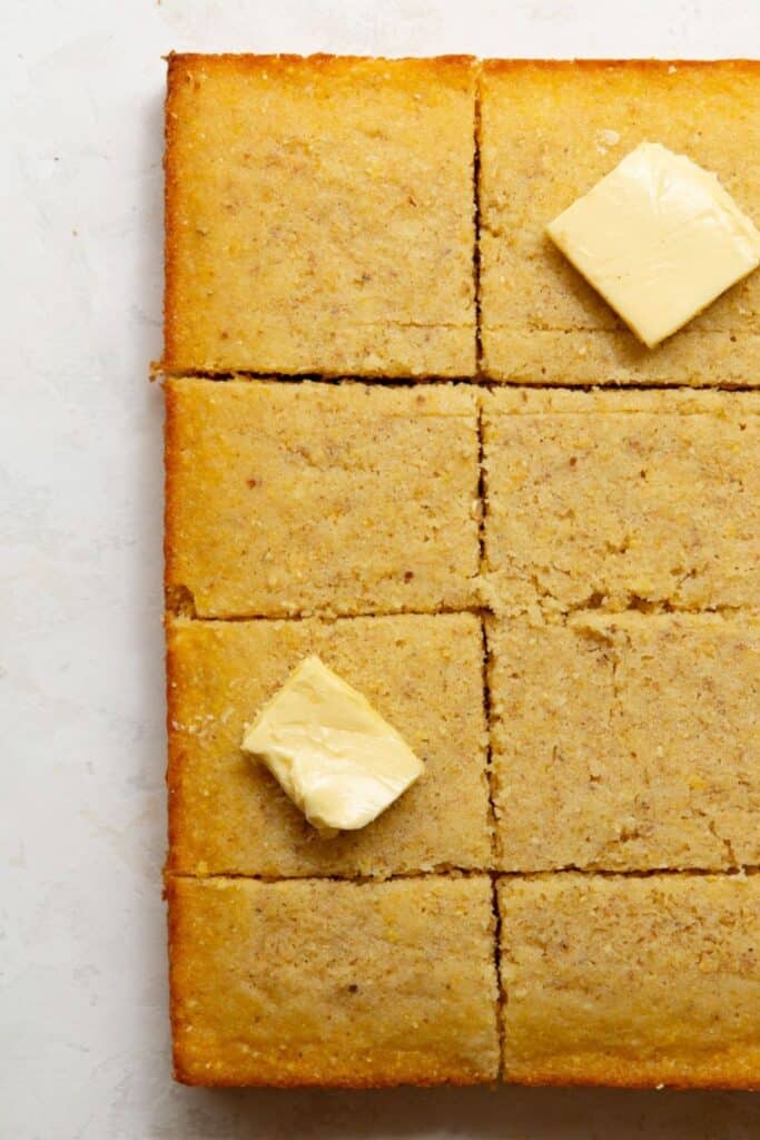 Gluten-free almond flour cornbread cut into squares with pats of butter.