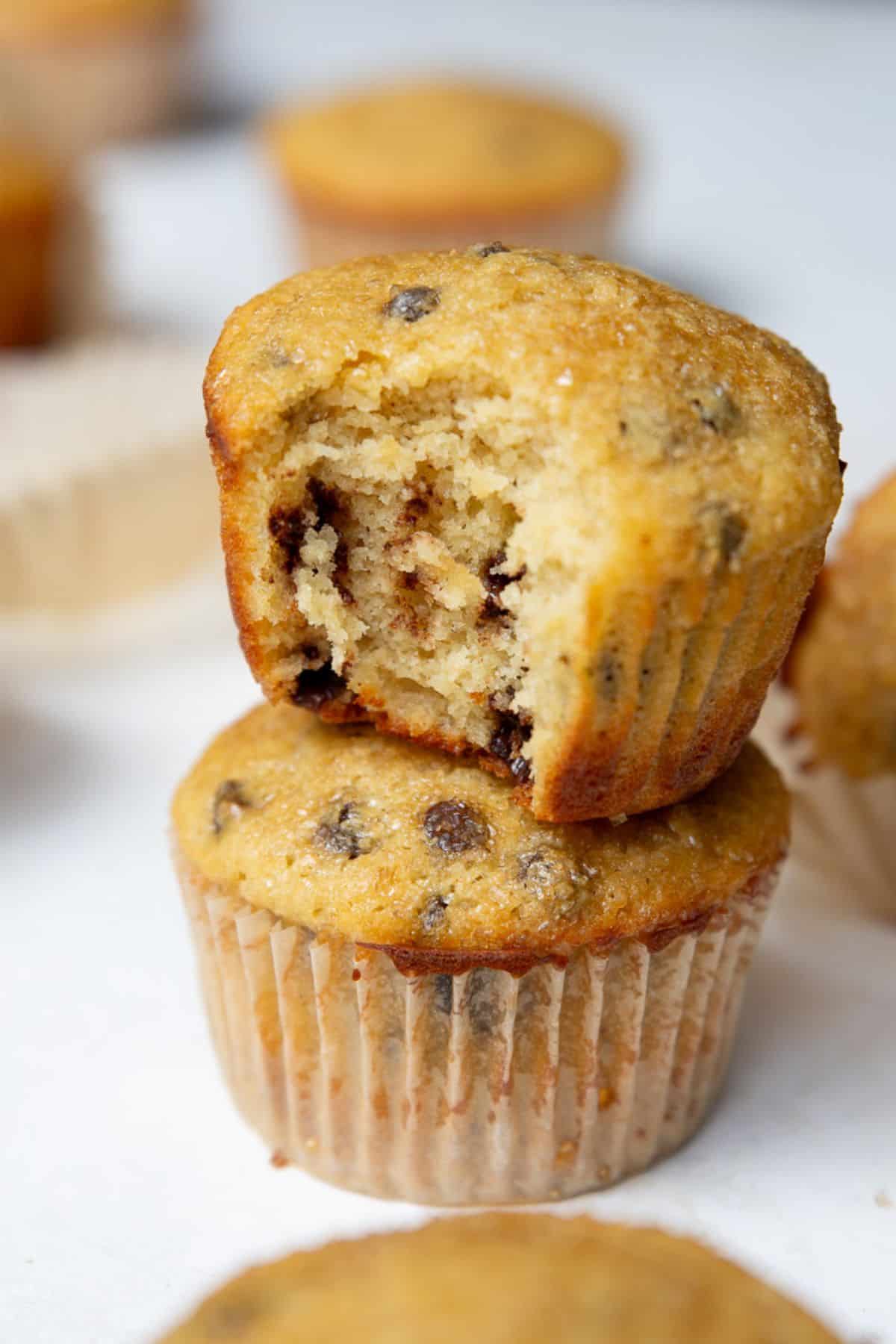 Two stacked chocolate chip protein muffins with the top one bitten to show the moist interior.