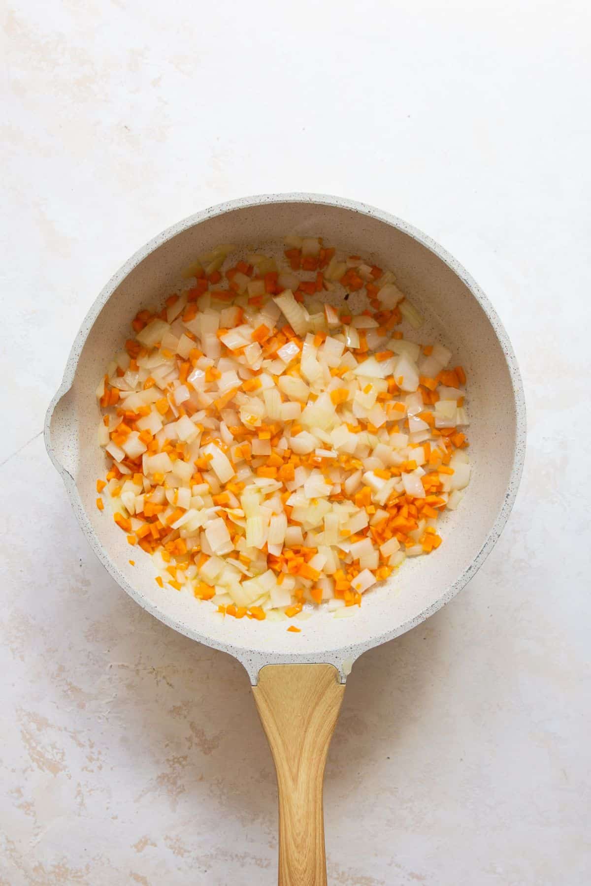 Diced carrot, onion, and bell pepper cooking in a skillet.