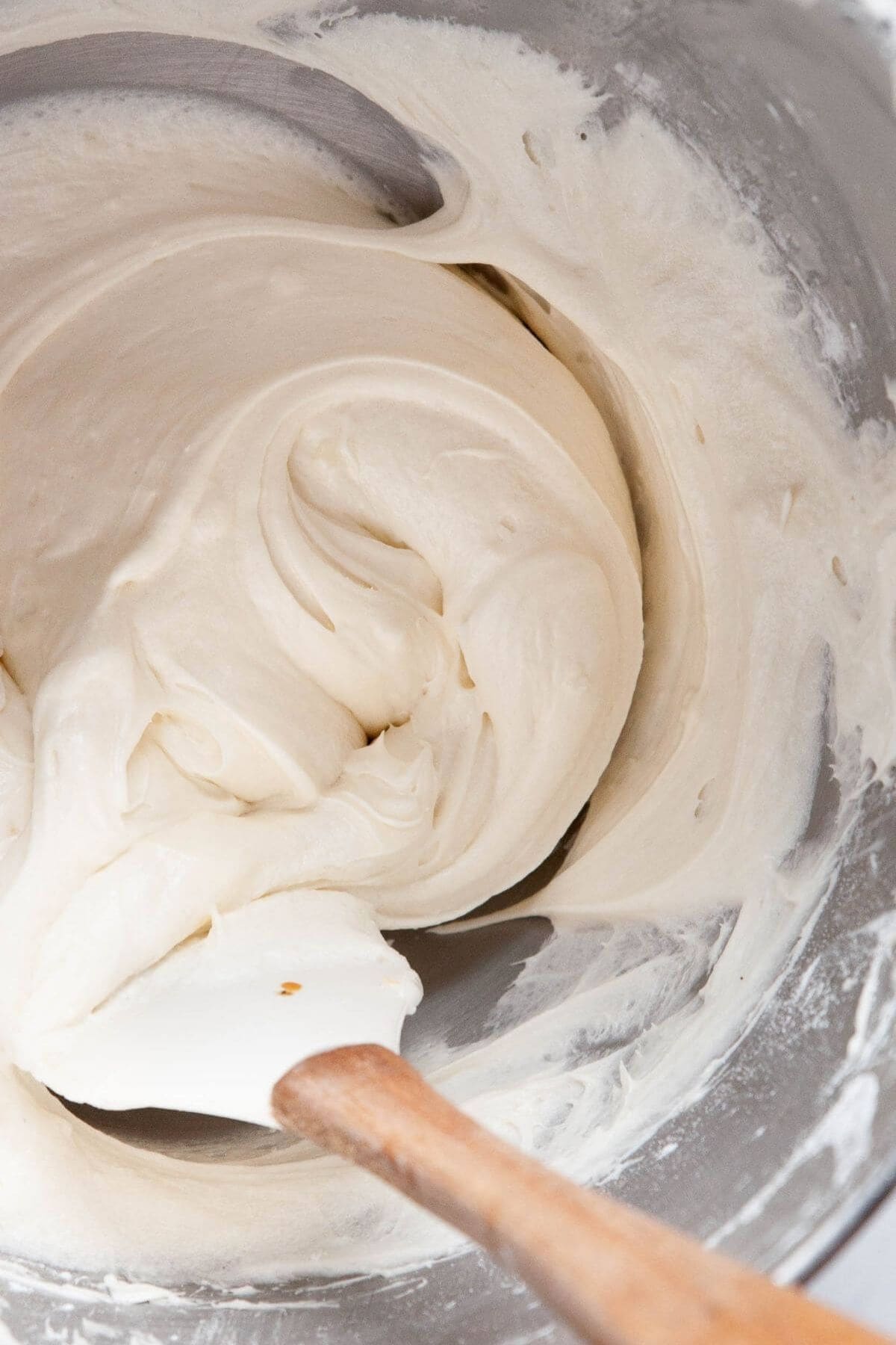 Whipped vanilla buttercream frosting in a mixing bowl with a spatula.
