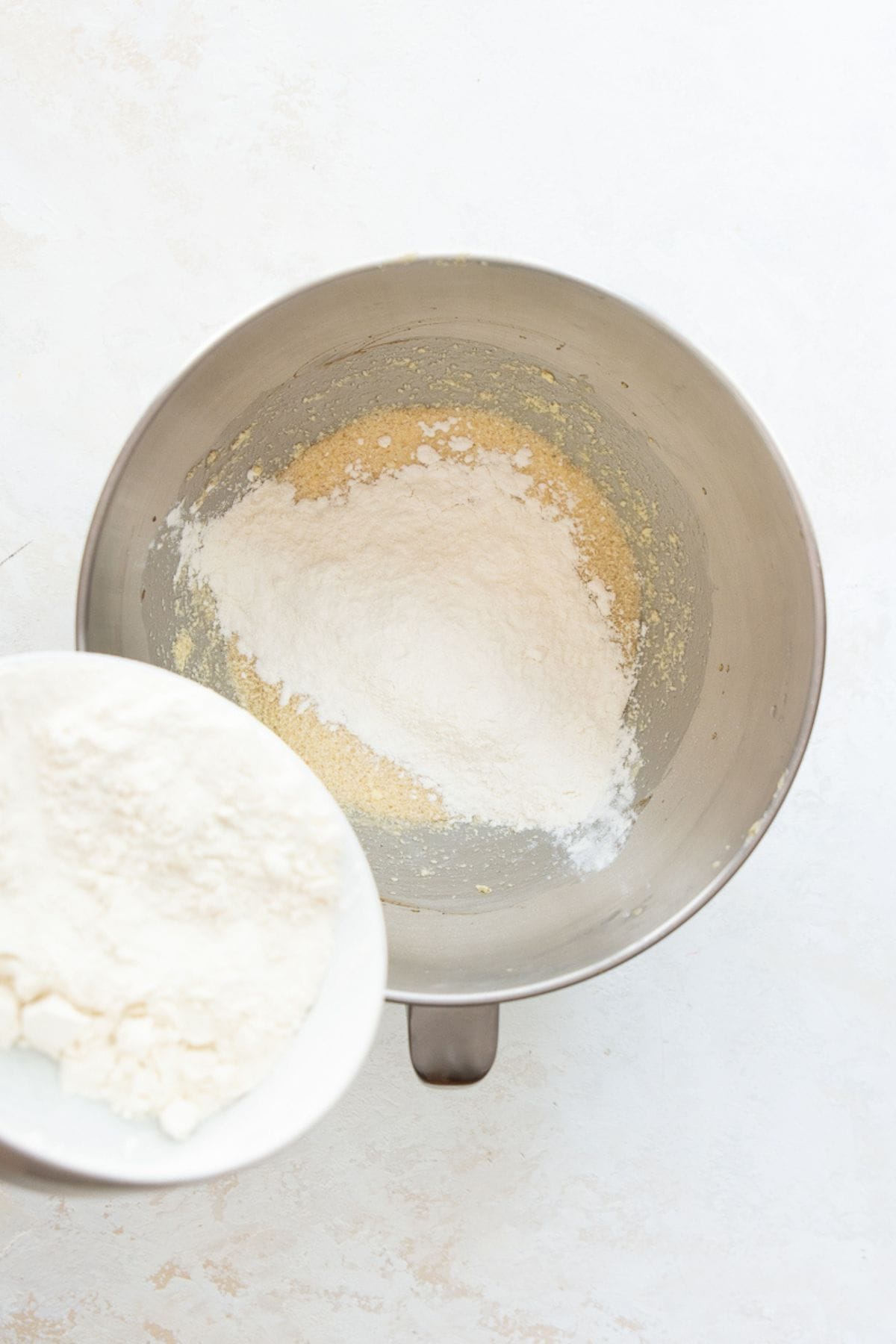 Flour mixture being added to the wet ingredients in a stand mixer bowl.