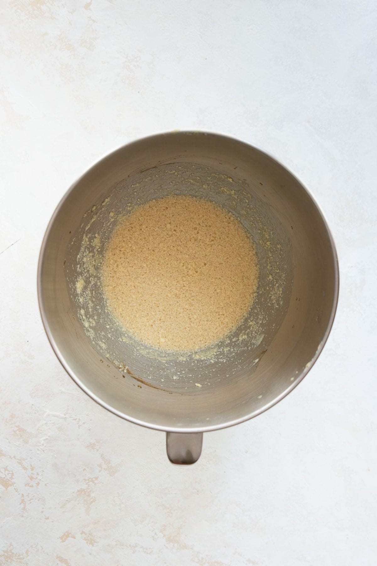 Butter and maple syrup beaten together in a stand mixer bowl, looking curdled and separated.