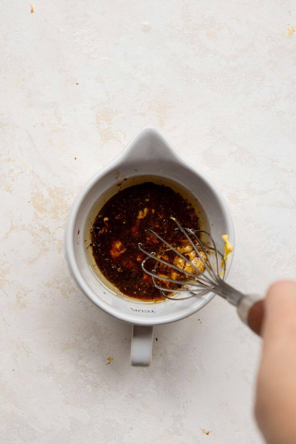 Whisking honey soy dressing with Dijon in a small bowl.