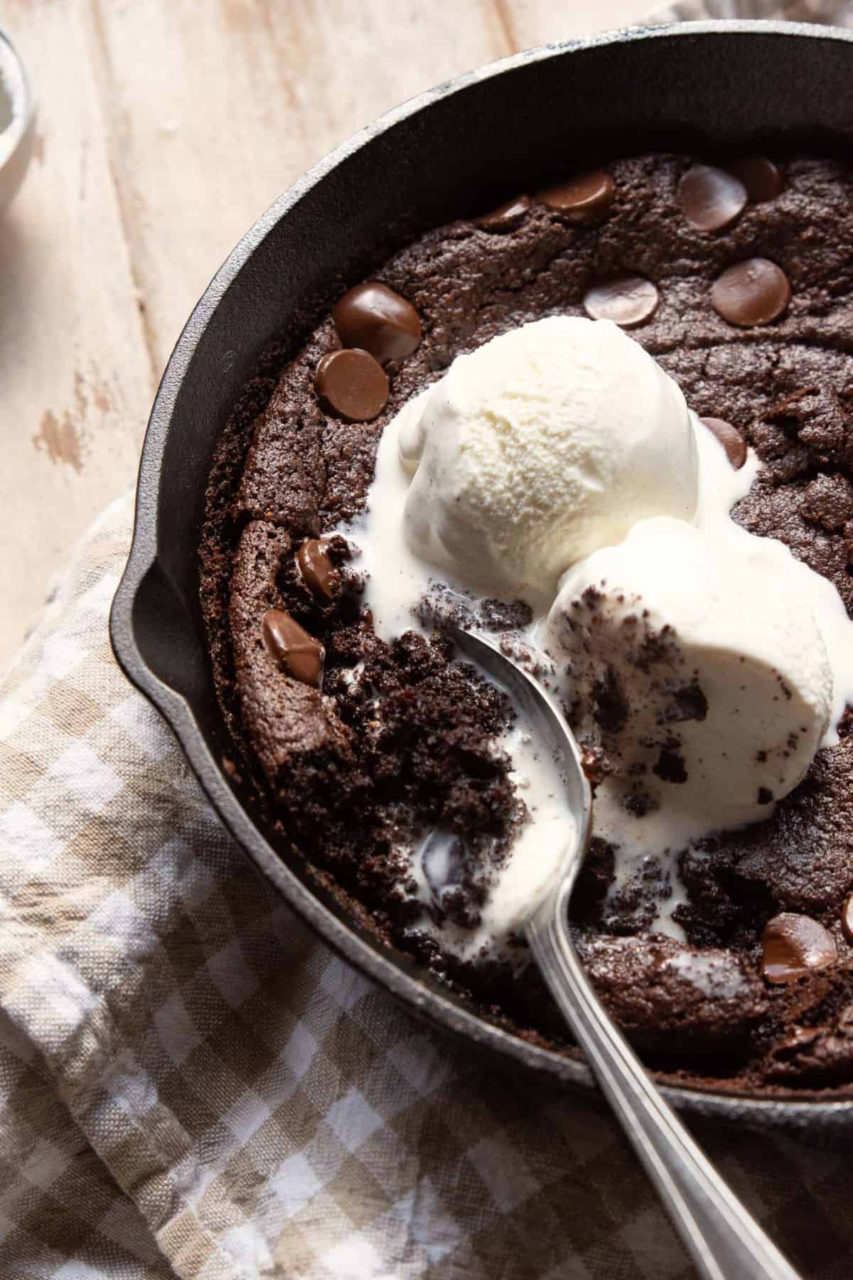Baked flourless brownie skillet with a crackly top and melted chocolate chips and ice cream.