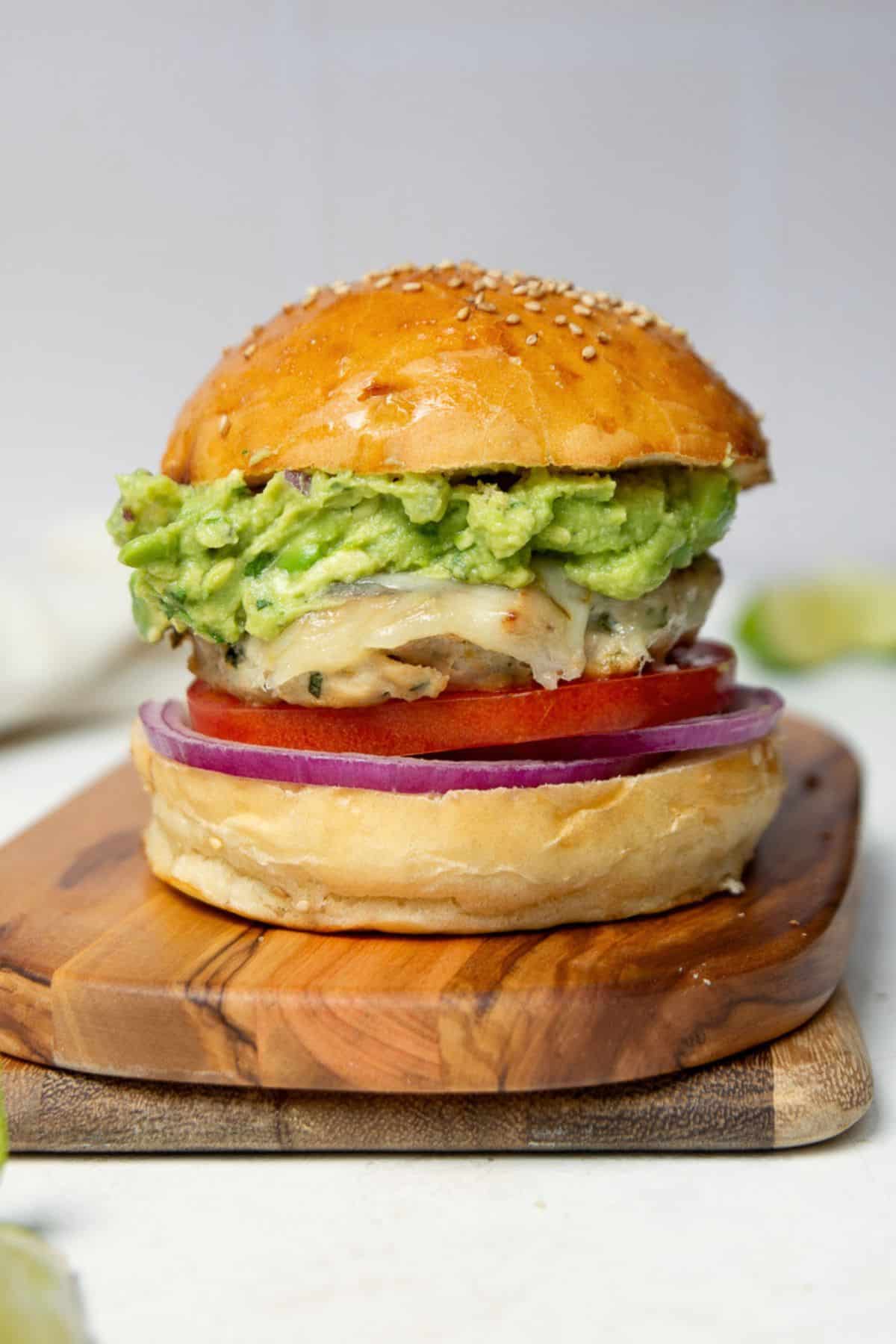 Juicy ground chicken burger on a sesame bun with guacamole, tomato, and red onion.