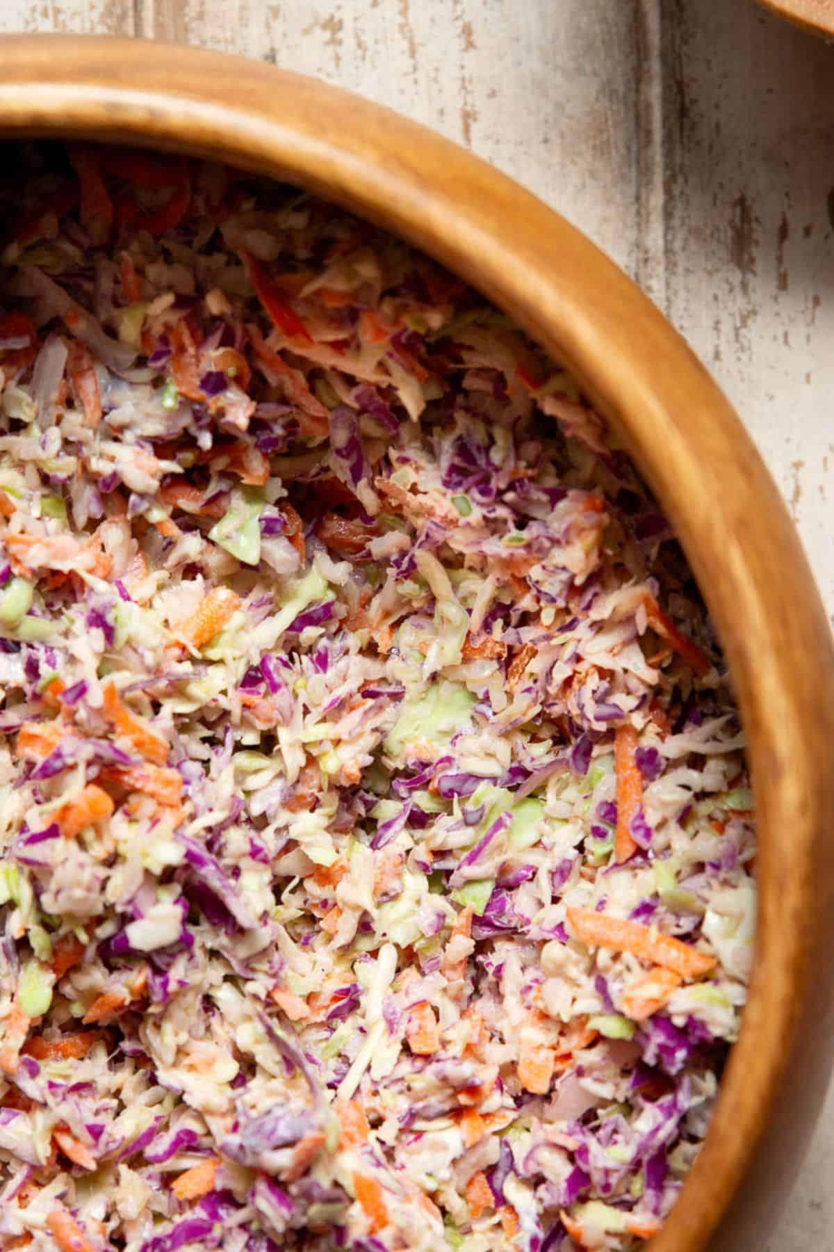 Low calorie coleslaw made with Greek yogurt, shredded cabbage, carrots, and red onion in a wooden bowl.
