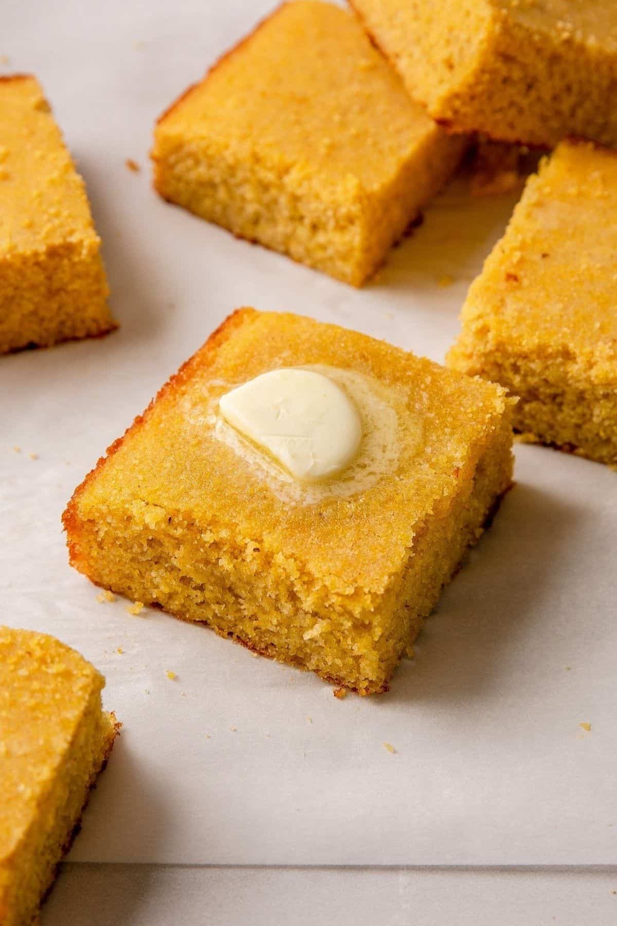 Moist almond flour cornbread square with melting butter on parchment.