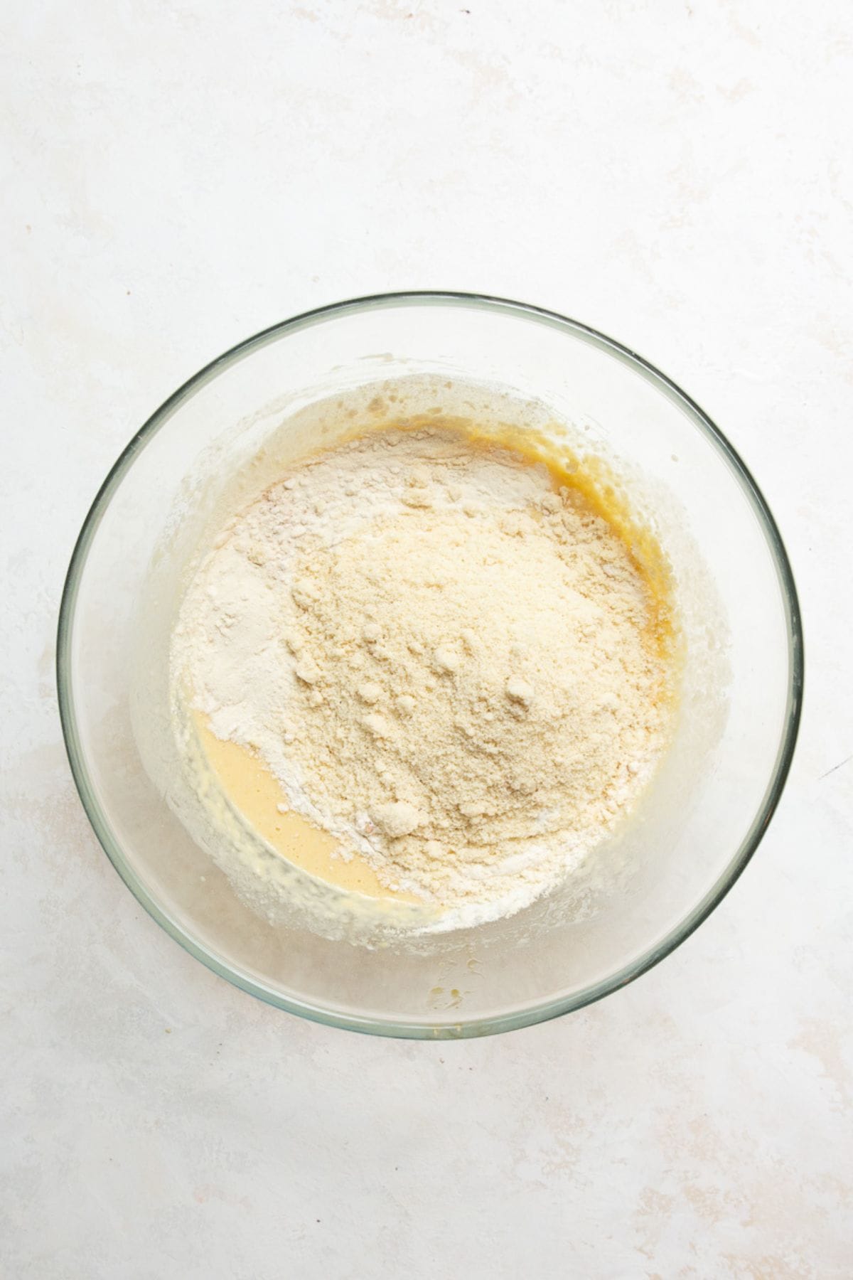 All-purpose flour, almond flour, and protein powder added on top of the wet ingredients in a glass bowl.