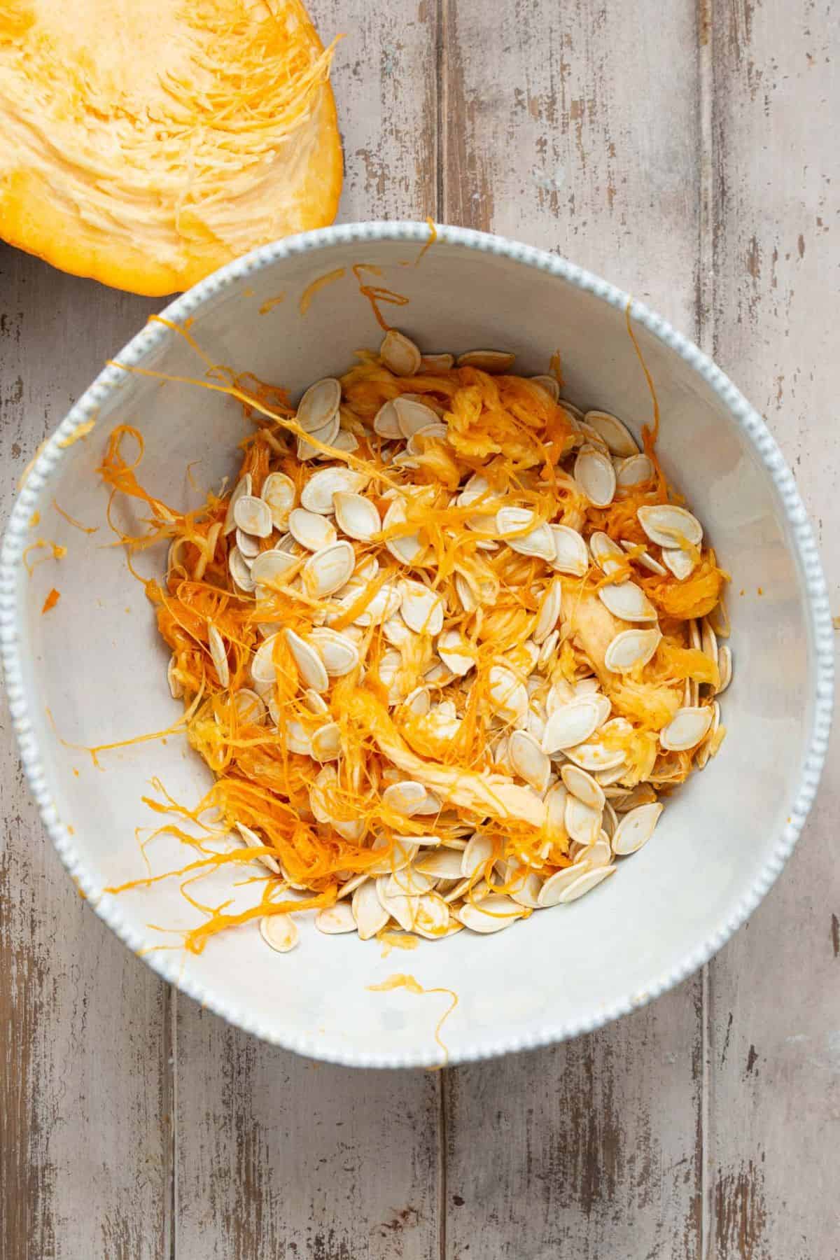 Raw pumpkin seeds in a bowl with pulp.