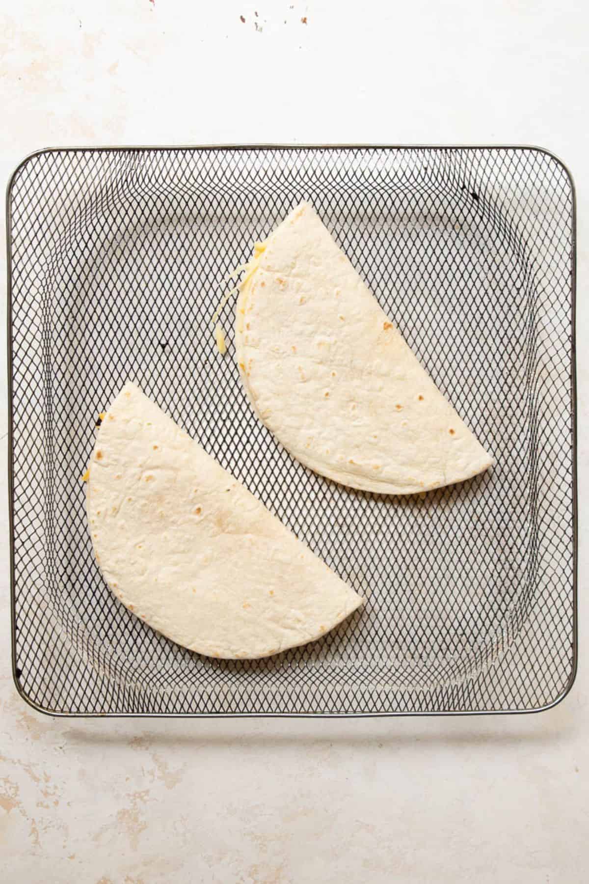 Two folded cheese quesadillas in an air fryer basket before cooking.