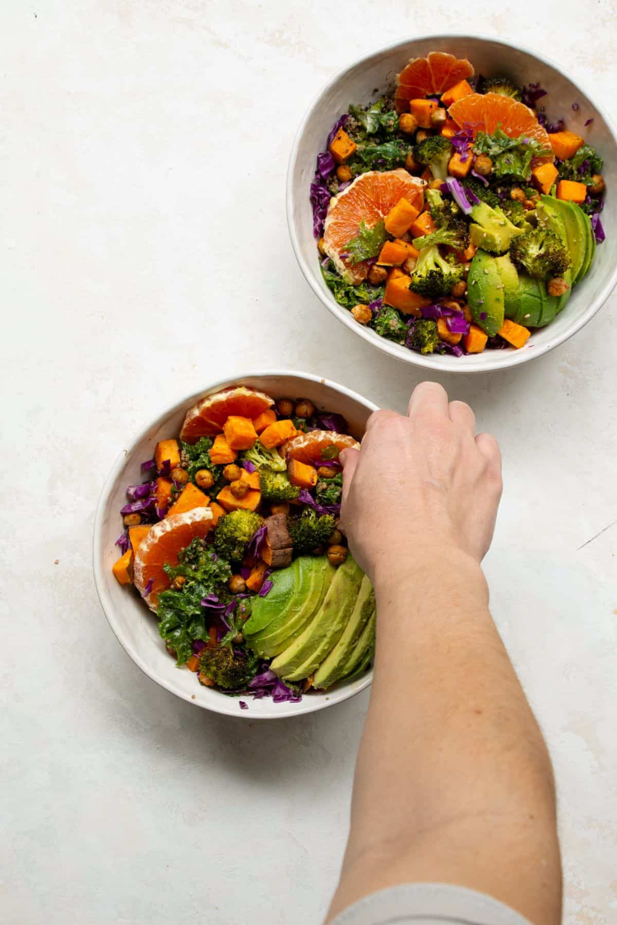 Assembling quinoa sweet potato bowls with avocado, orange slices, and red cabbage.