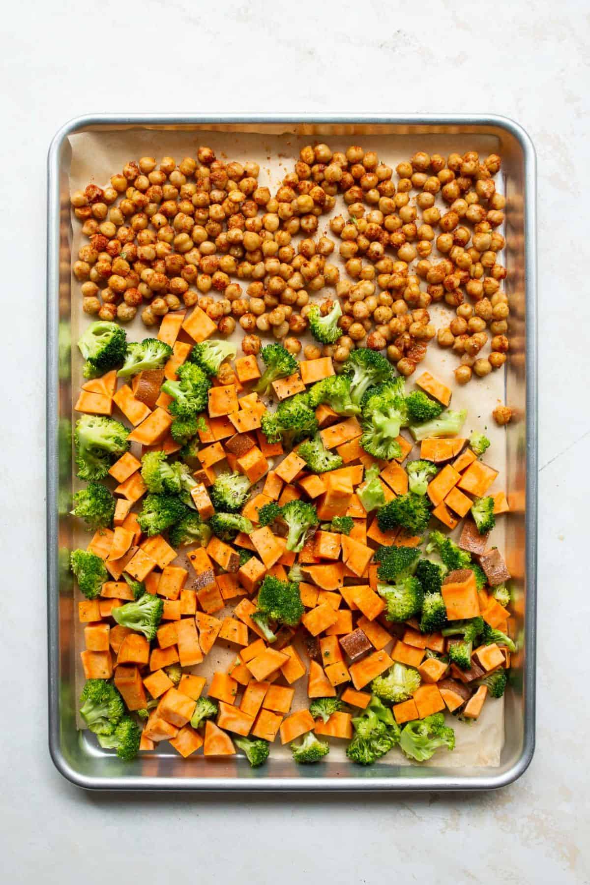 Seasoned chickpeas added to one third of the sheet pan beside sweet potatoes and broccoli.