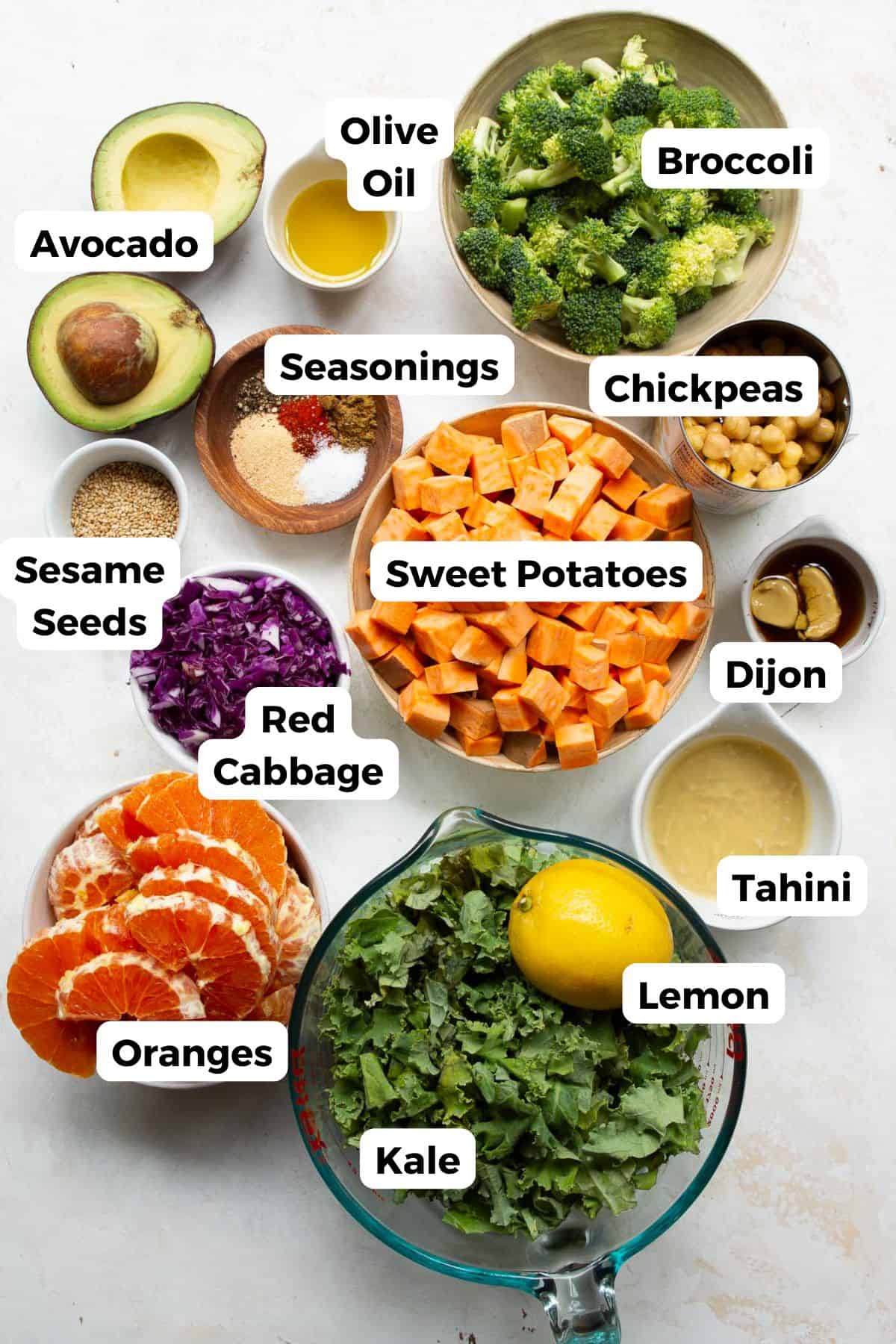Ingredients for a quinoa sweet potato bowl including sweet potatoes, broccoli, chickpeas, kale, red cabbage, oranges, avocado, and tahini.