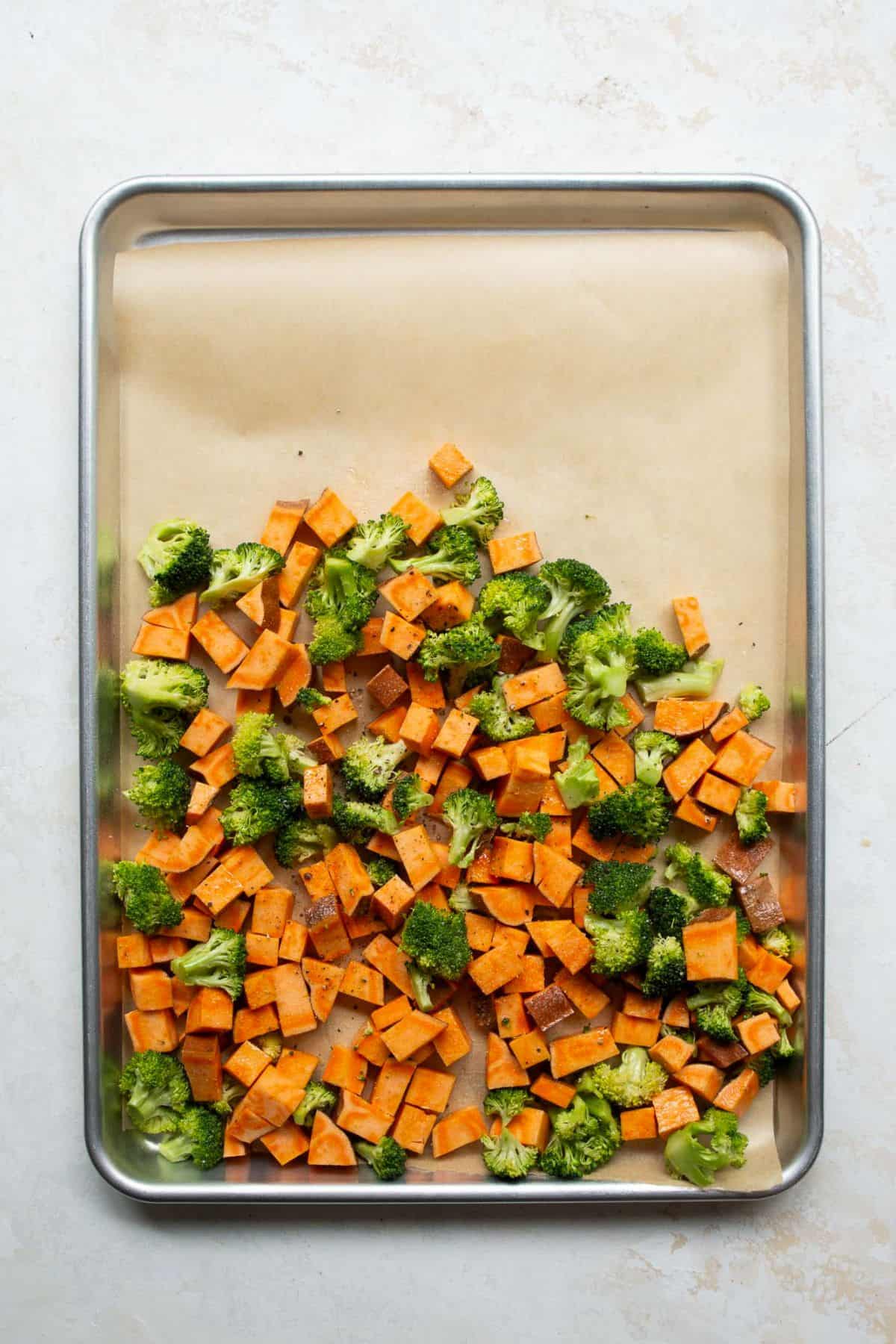 Cubed sweet potatoes and broccoli florets spread on a parchment-lined sheet pan.