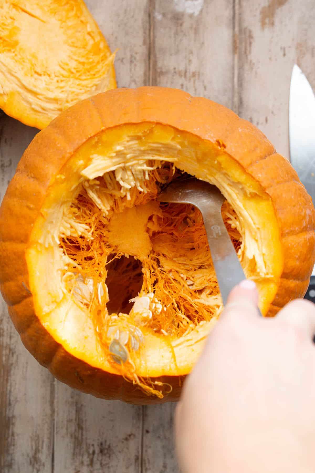 Scooping seeds out of a cut open pumpkin with a spoon.
