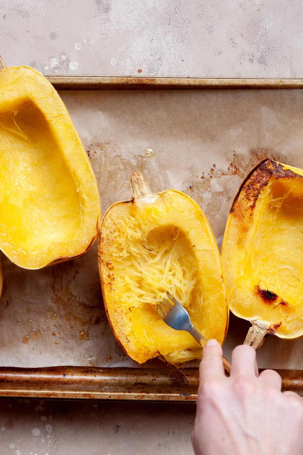 Scraping roasted spaghetti squash into strands with a fork, leaving a border of squash in the shell.