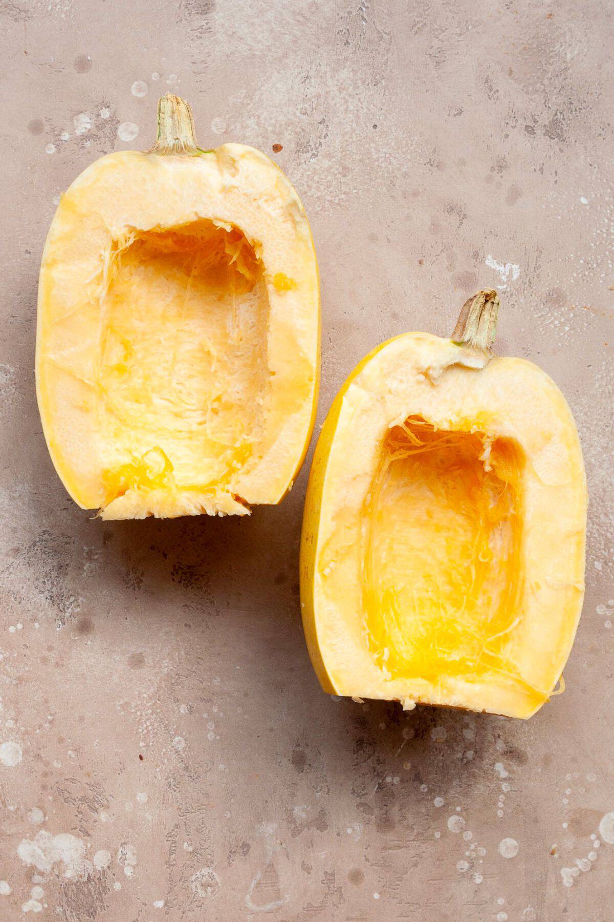 Two raw spaghetti squash halves with the seeds removed on a stone counter.