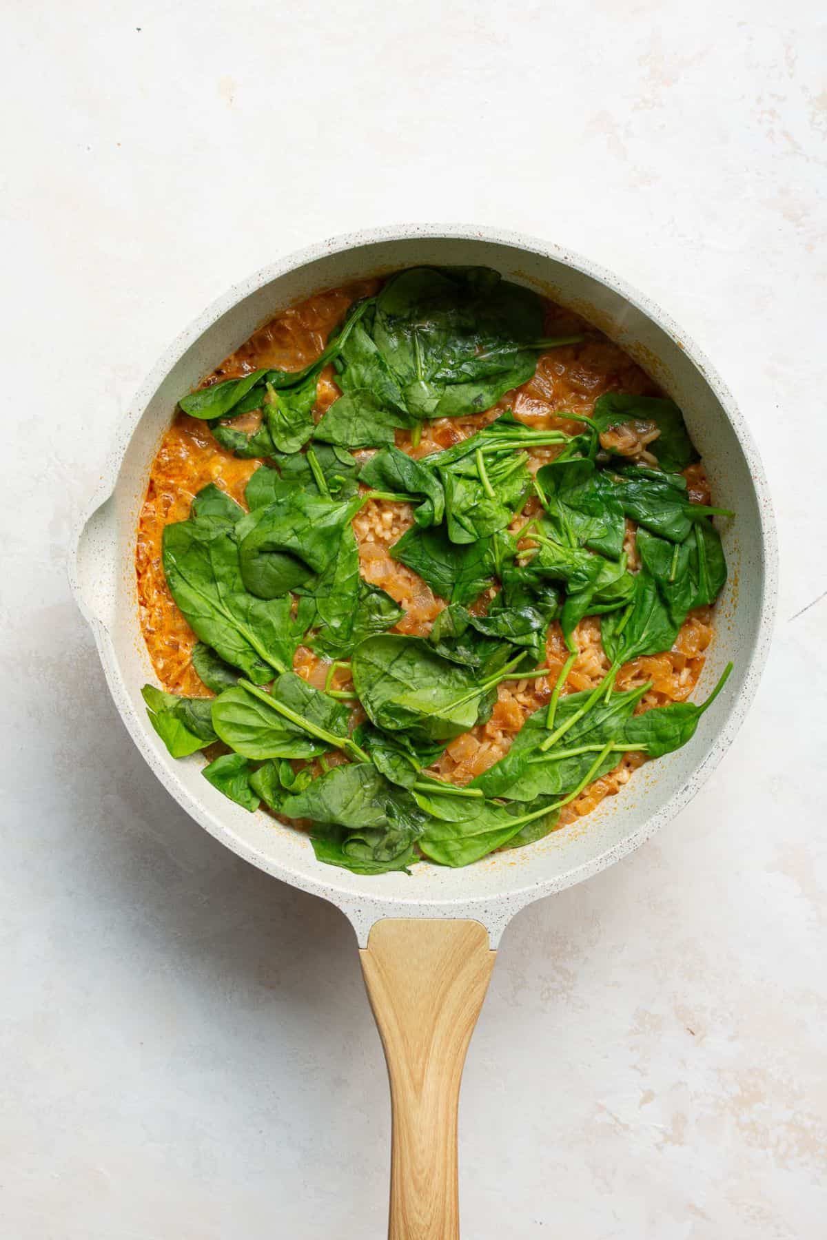 Fresh baby spinach layered on top of cooked lemon rice in a covered skillet.