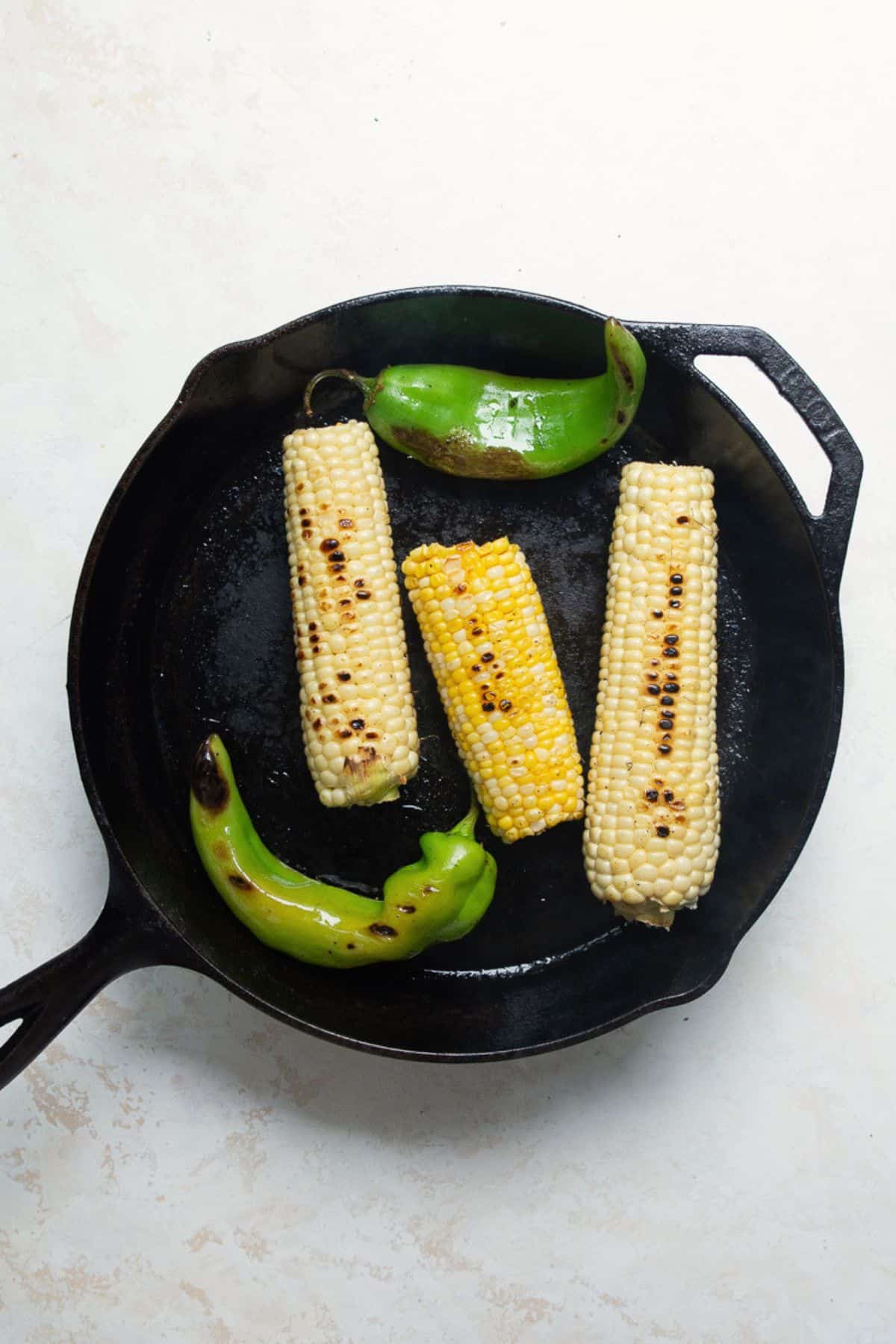 Corn on the cob and whole jalapeños charring in a cast iron skillet.
