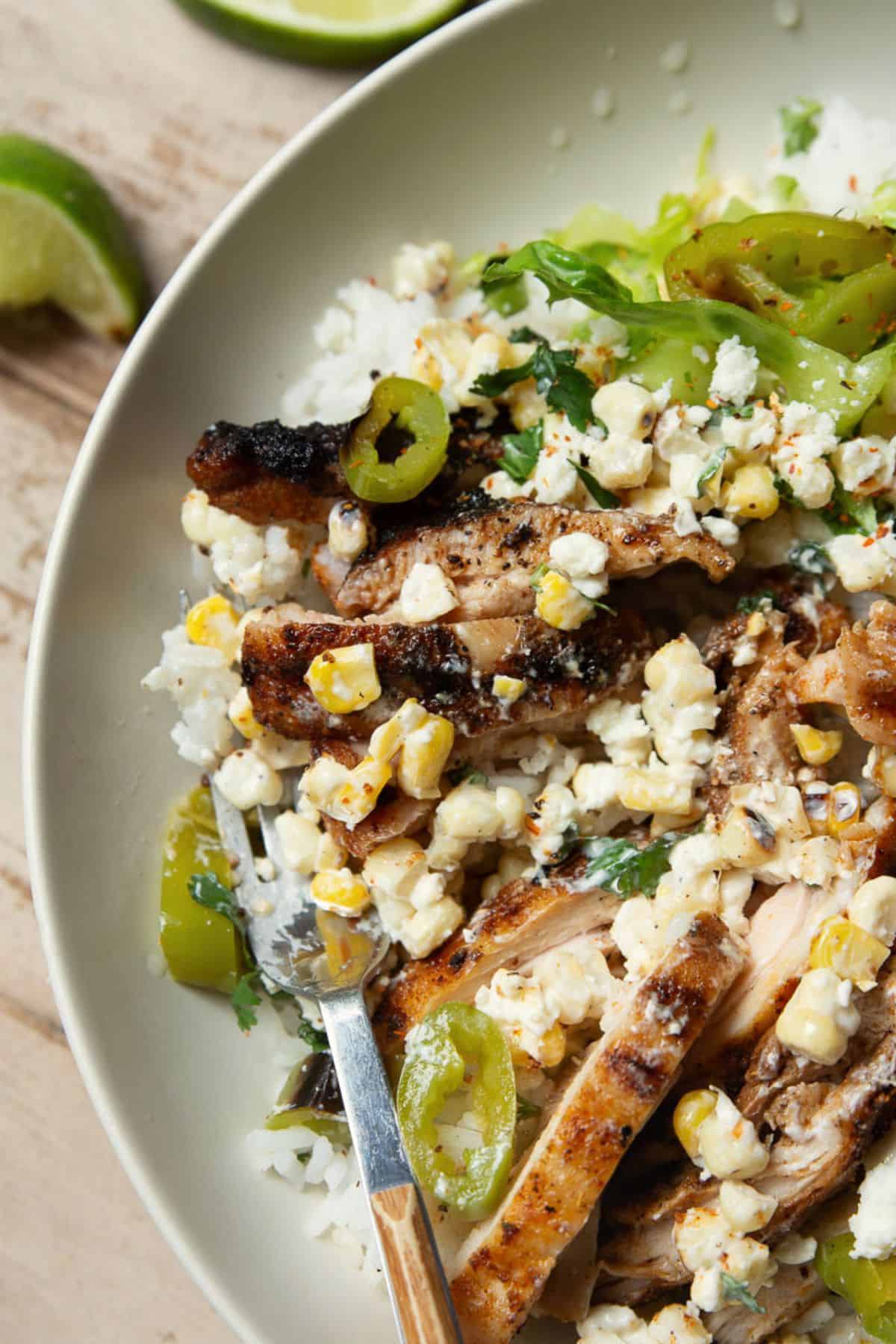 Close view of grilled chicken and esquites corn topping over white rice.