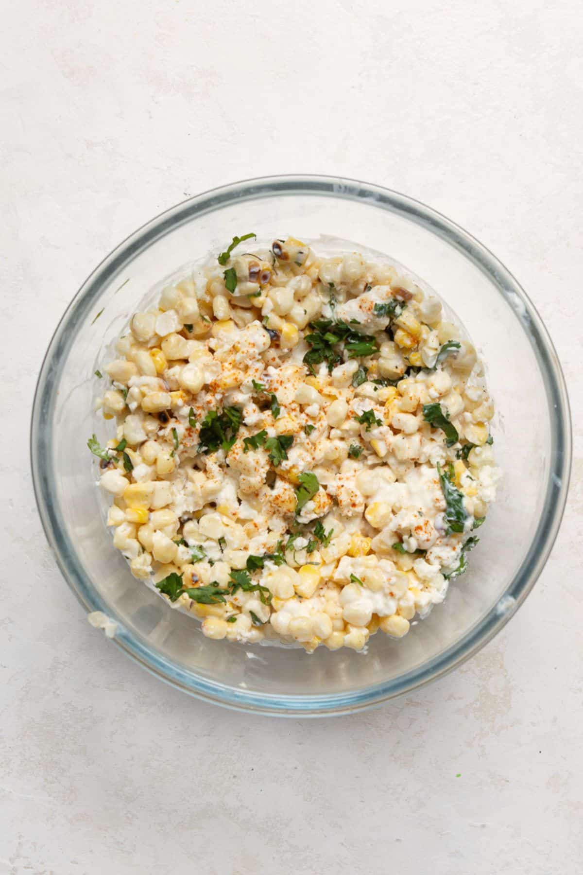 Esquites-style street corn topping with Greek yogurt, cotija, cilantro, and chili powder in a glass bowl.