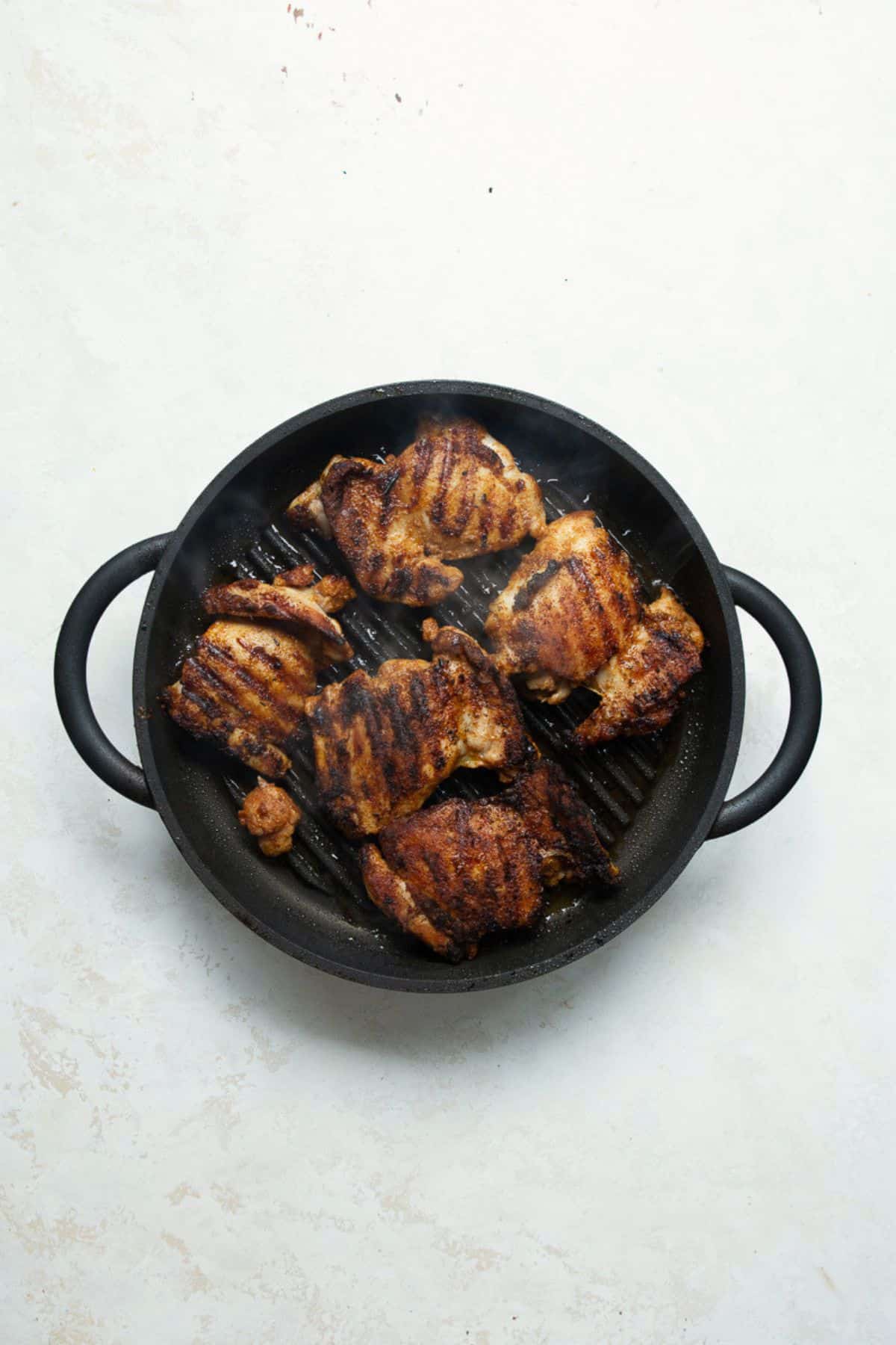Seasoned chicken thighs with grill marks in a cast iron grill pan.