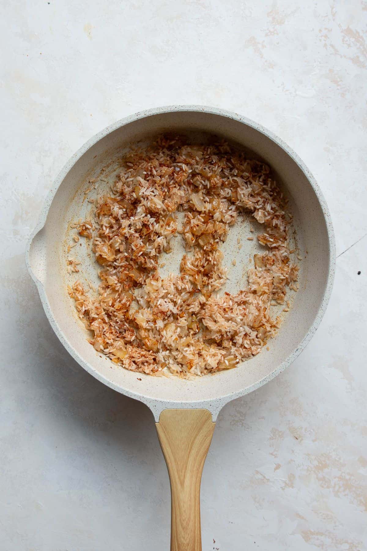 Jasmine rice toasting with onion, garlic, and paprika in a skillet.