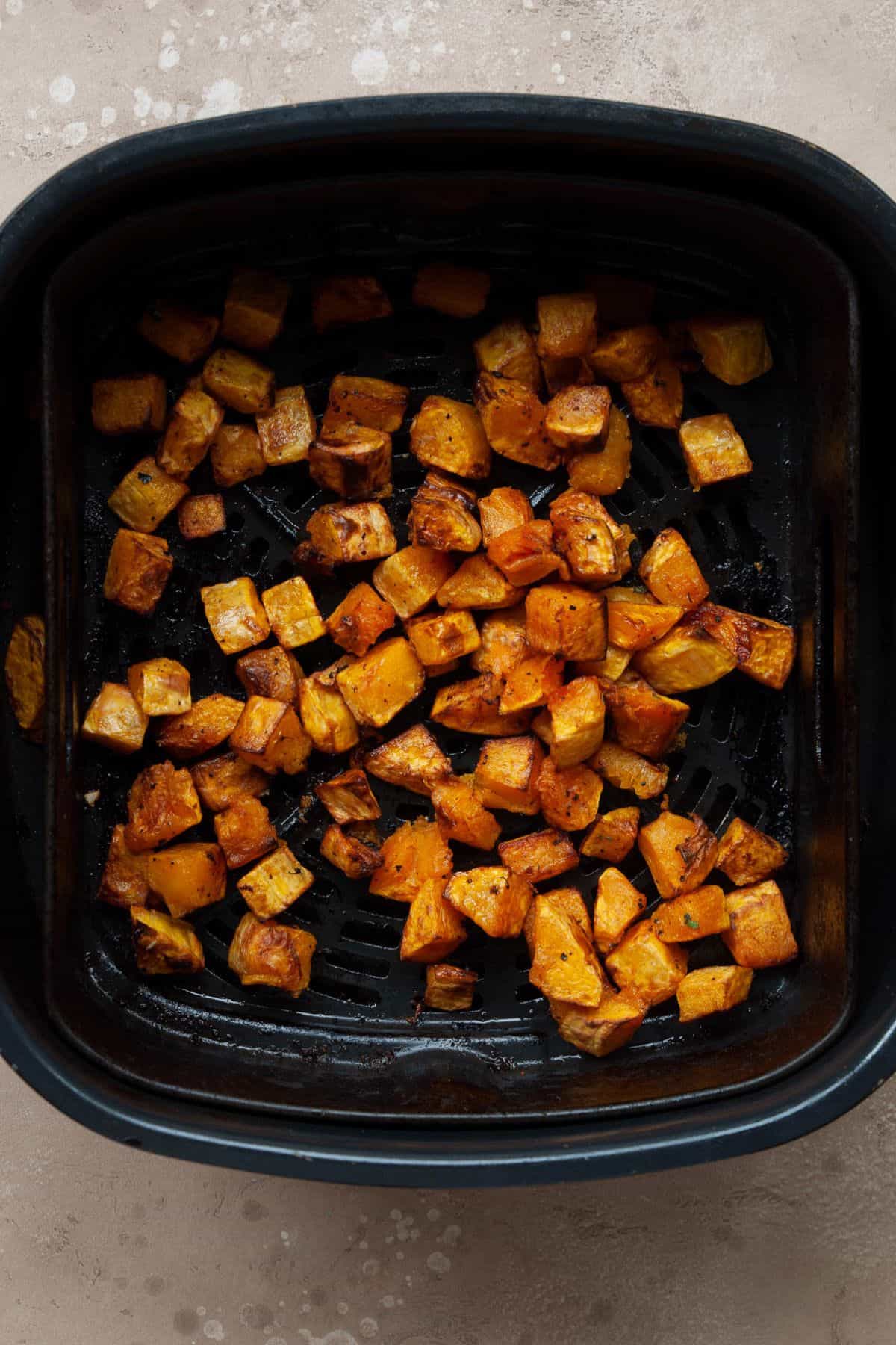 Air fryer butternut squash cubes with caramelized golden brown edges in the air fryer basket.