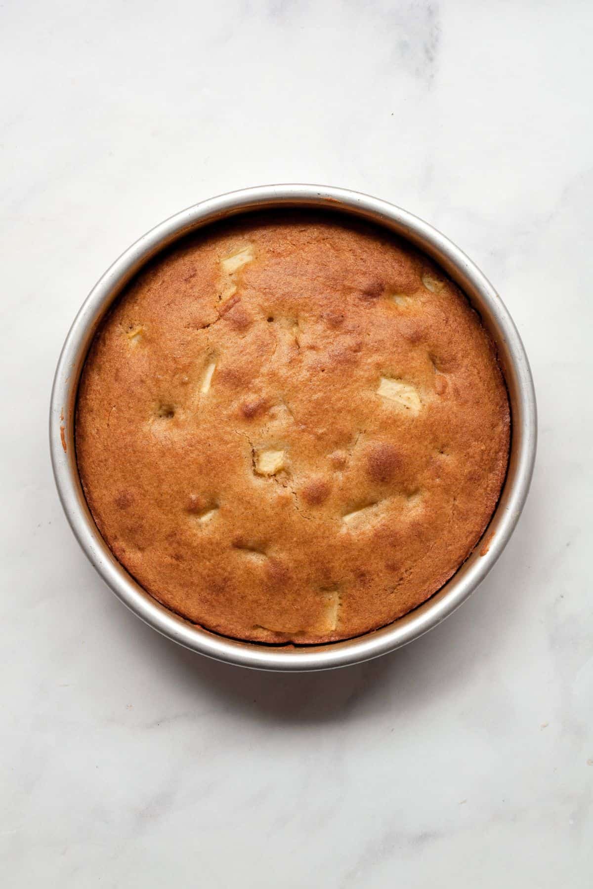 Golden baked gluten-free apple cake with apple pieces on top, cooling in a round pan.