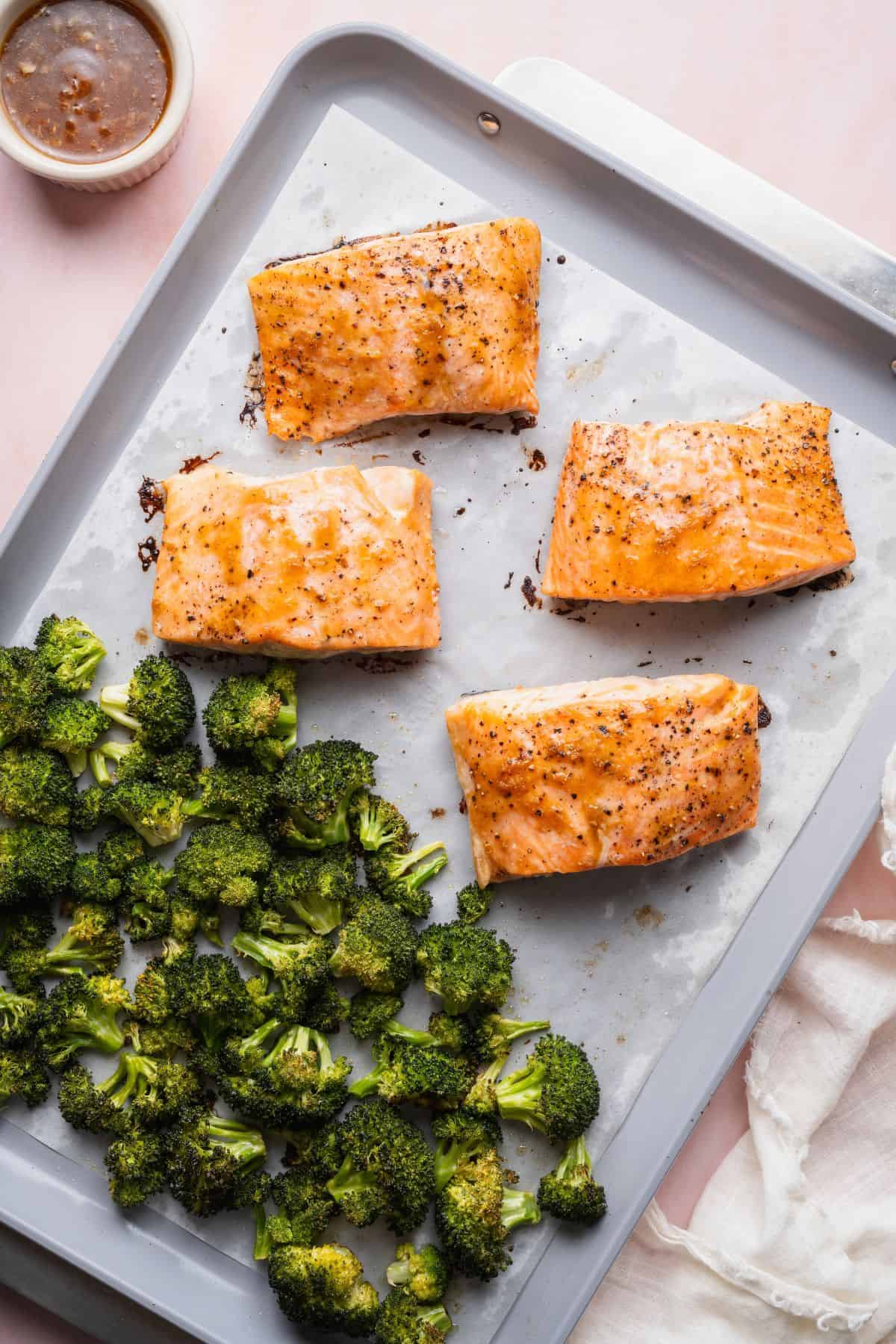 Baked teriyaki-glazed salmon fillets and crispy roasted broccoli on a parchment-lined sheet pan.