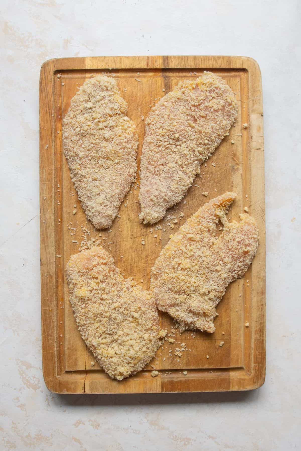 Four breaded chicken cutlets on a wooden cutting board, ready for the air fryer.