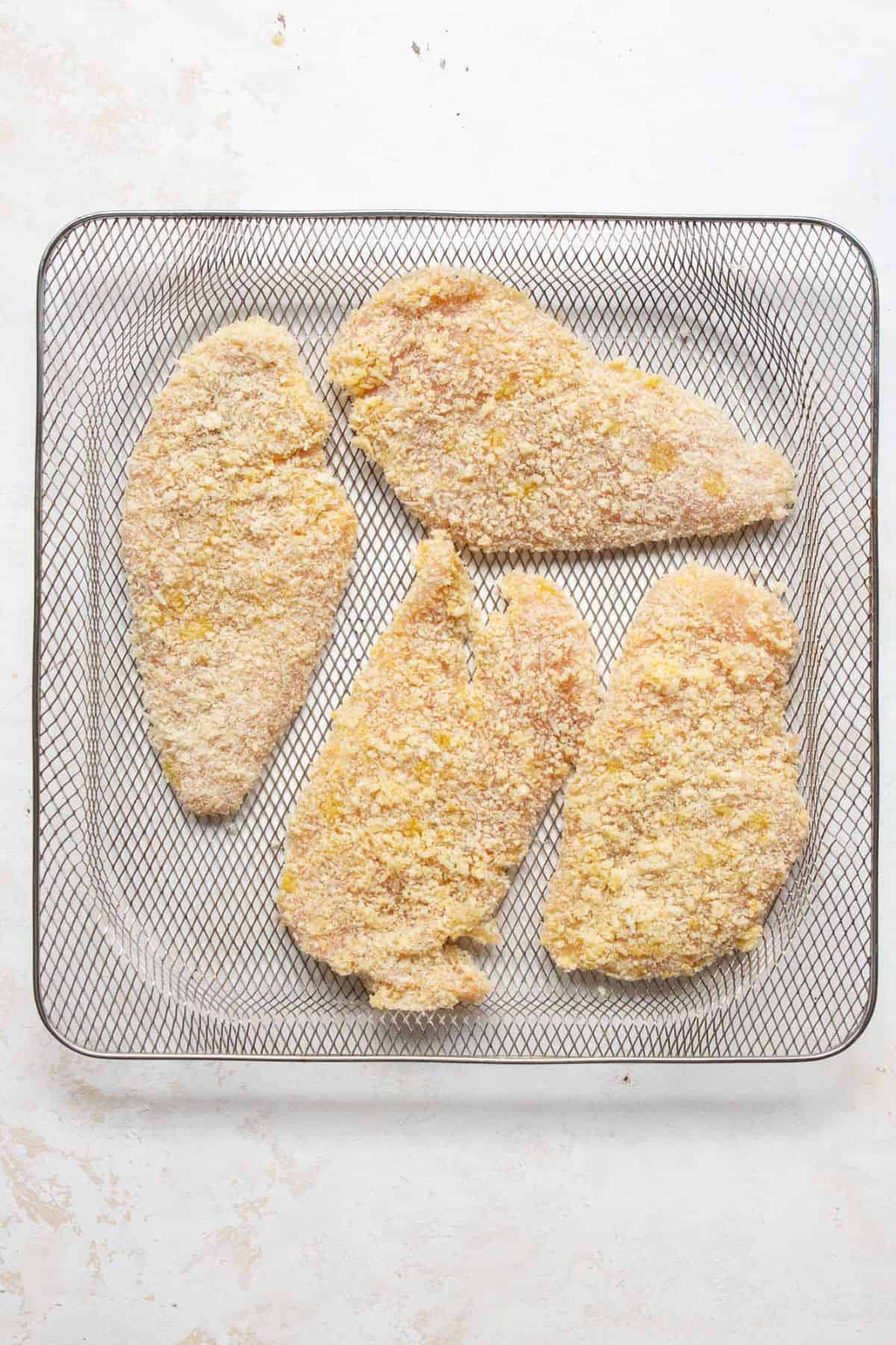 Breaded chicken cutlets in a single layer in an air fryer basket.